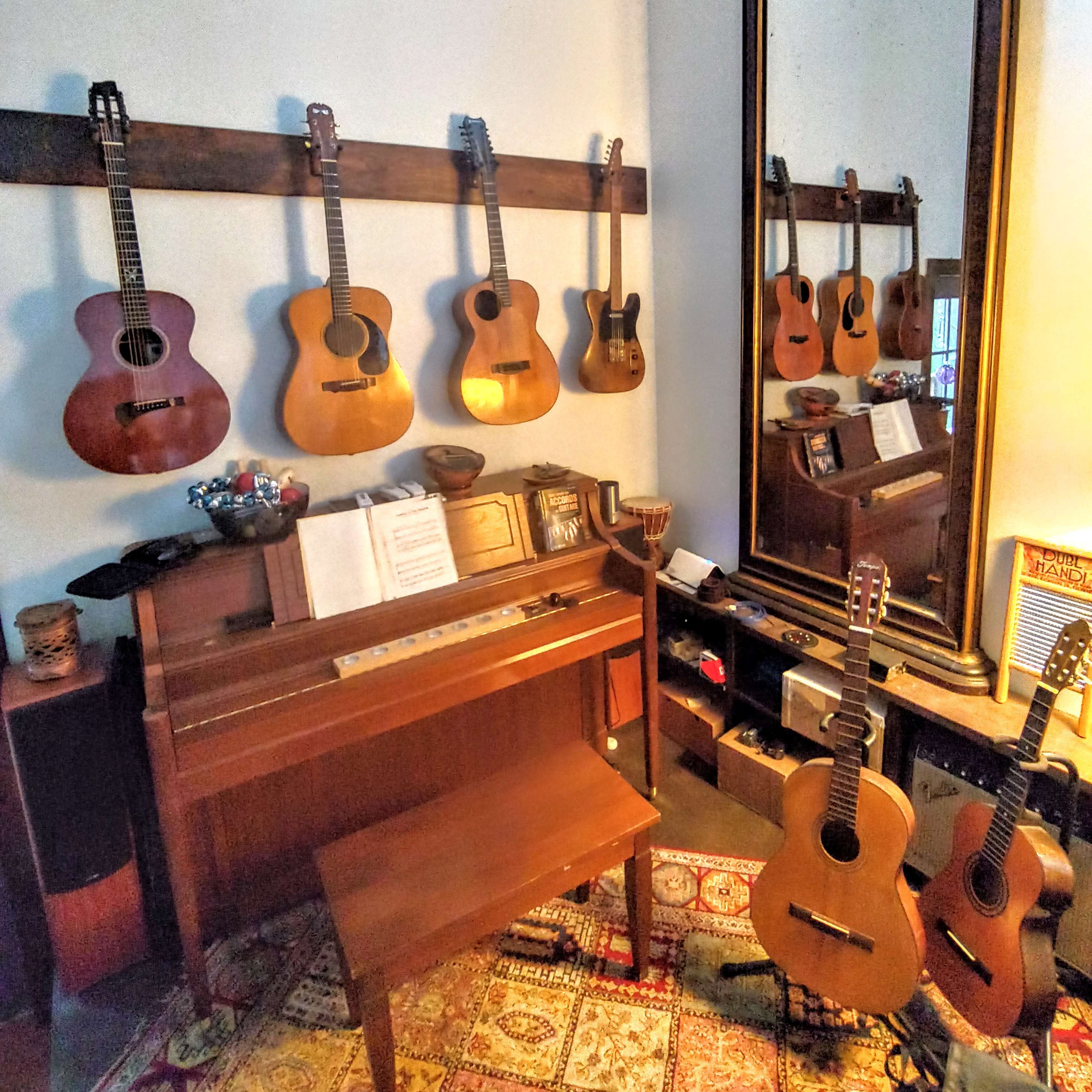 The scene features a wooden piano with an open sheet music book and several guitars displayed on the wall and leaning against furniture in a cozy room.