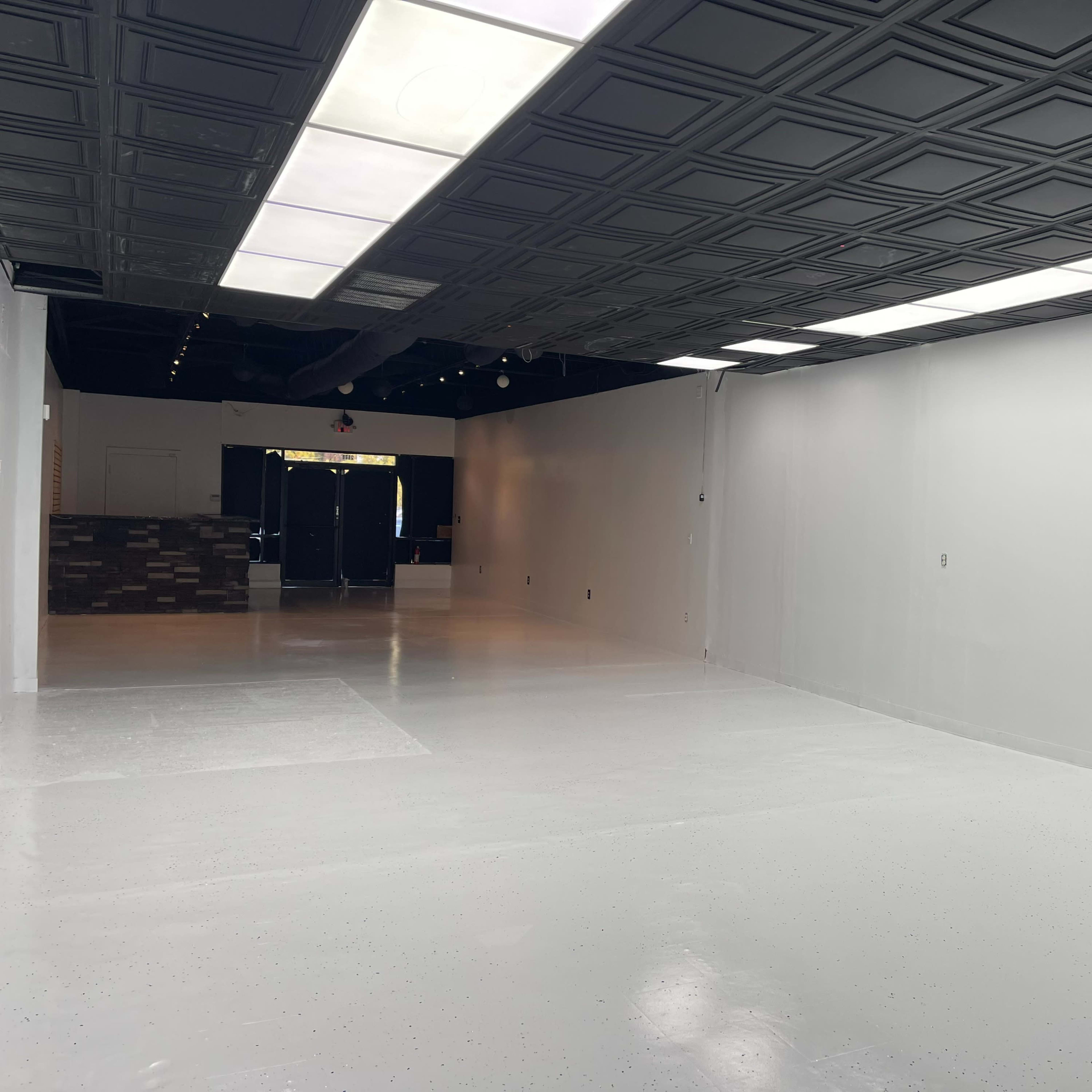 An empty, well-lit commercial space with white walls and a glossy floor, featuring a textured ceiling.