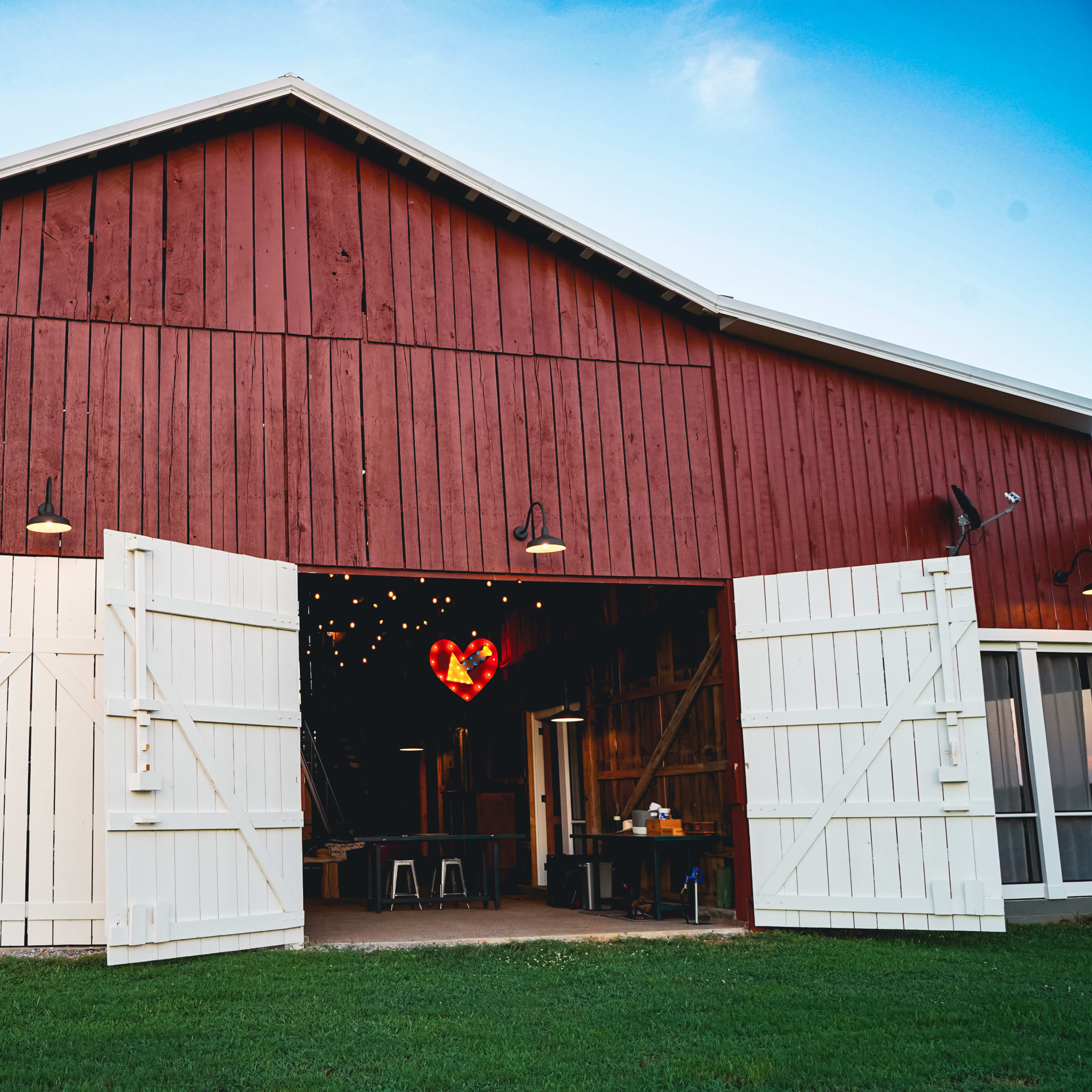 A red barn with white double doors is open, revealing a heart-shaped light fixture hanging inside.