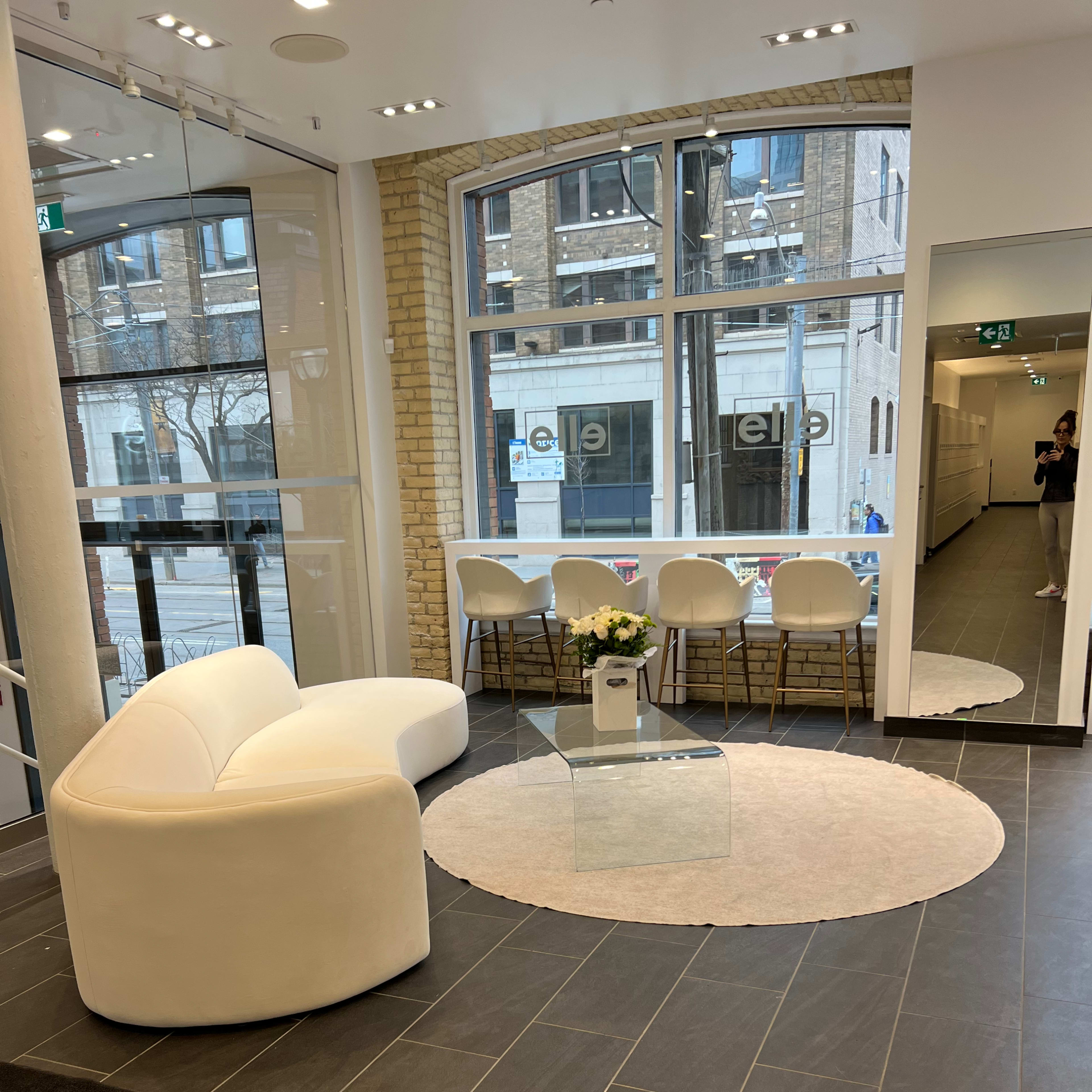 A modern lobby area with a white curved sofa, a round rug, a glass coffee table, and a seating arrangement featuring white chairs.