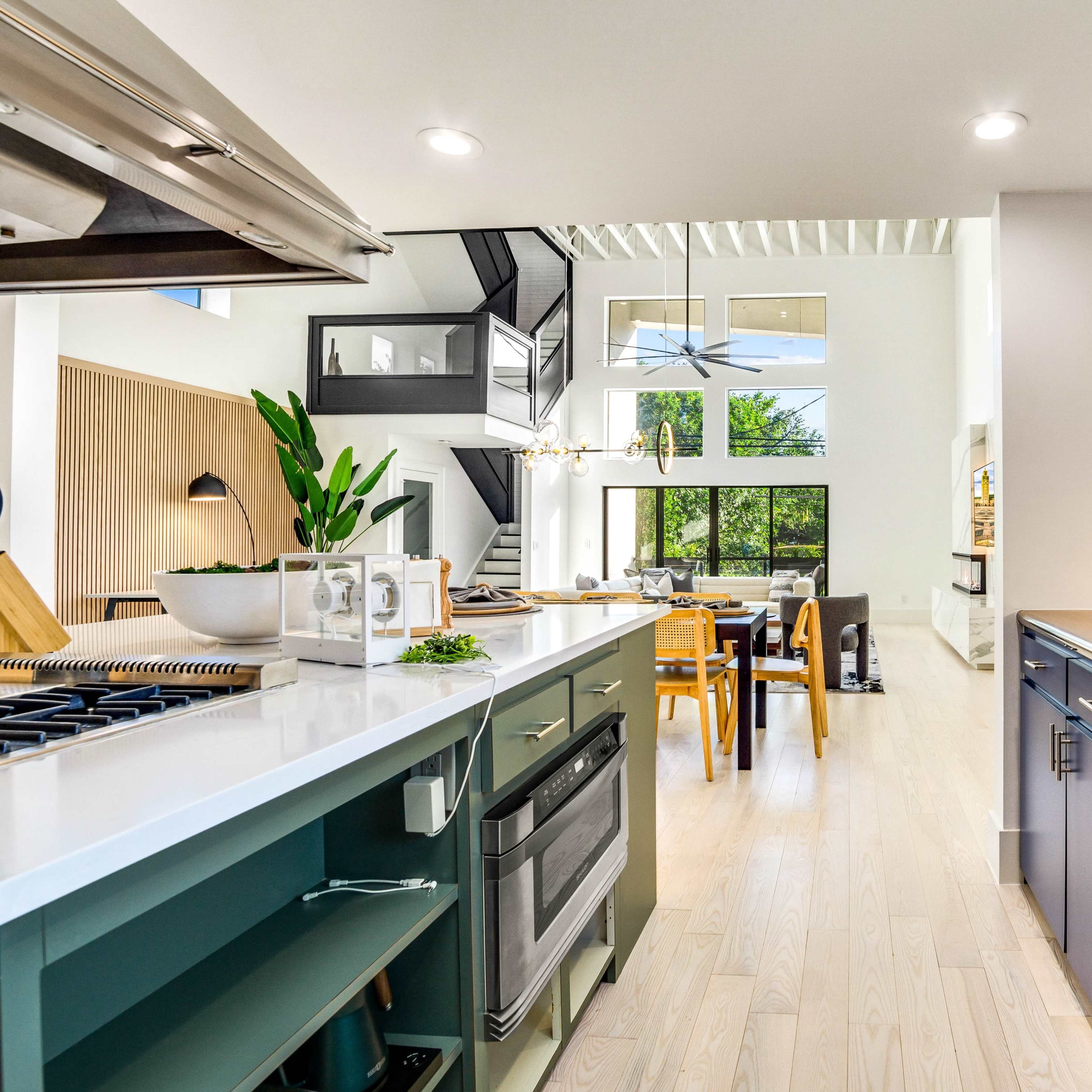 A modern kitchen features a stainless steel stove, blue cabinetry, and a view of a dining area with large windows.