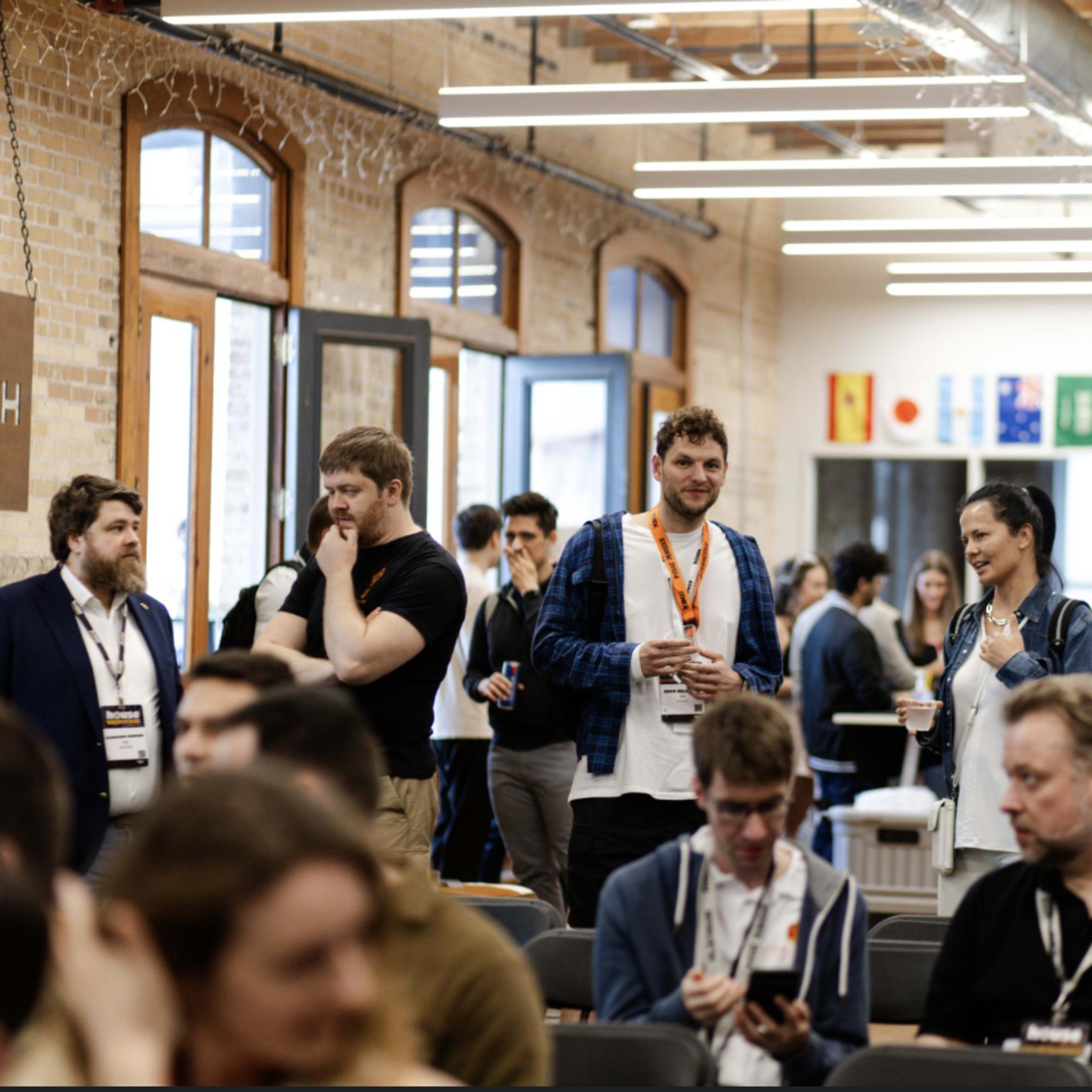 A diverse group of people interacts and mingles in a spacious event venue decorated with flags.