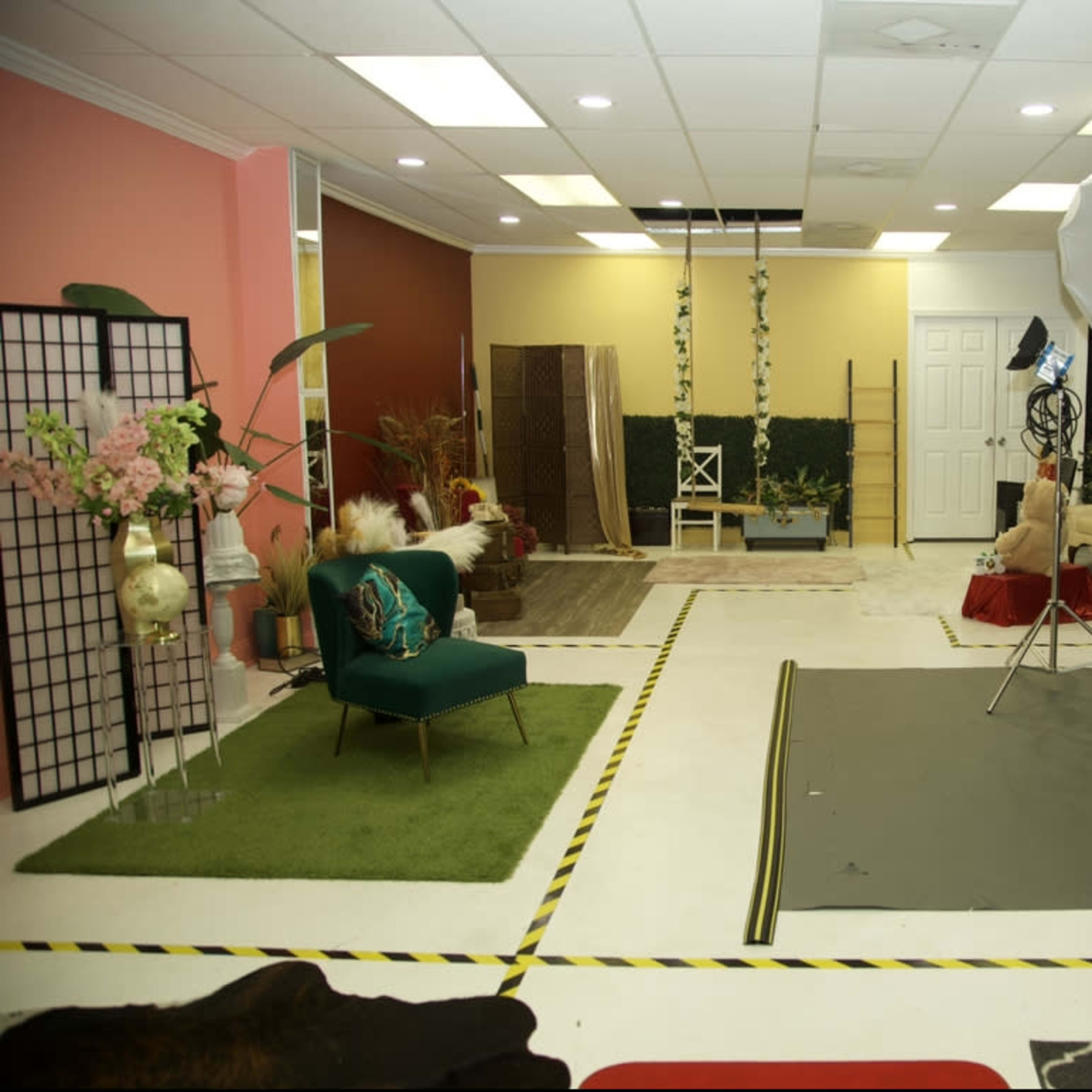 A photography studio featuring various backdrops, a green sofa, lighting equipment, and decorative elements arranged across the space.