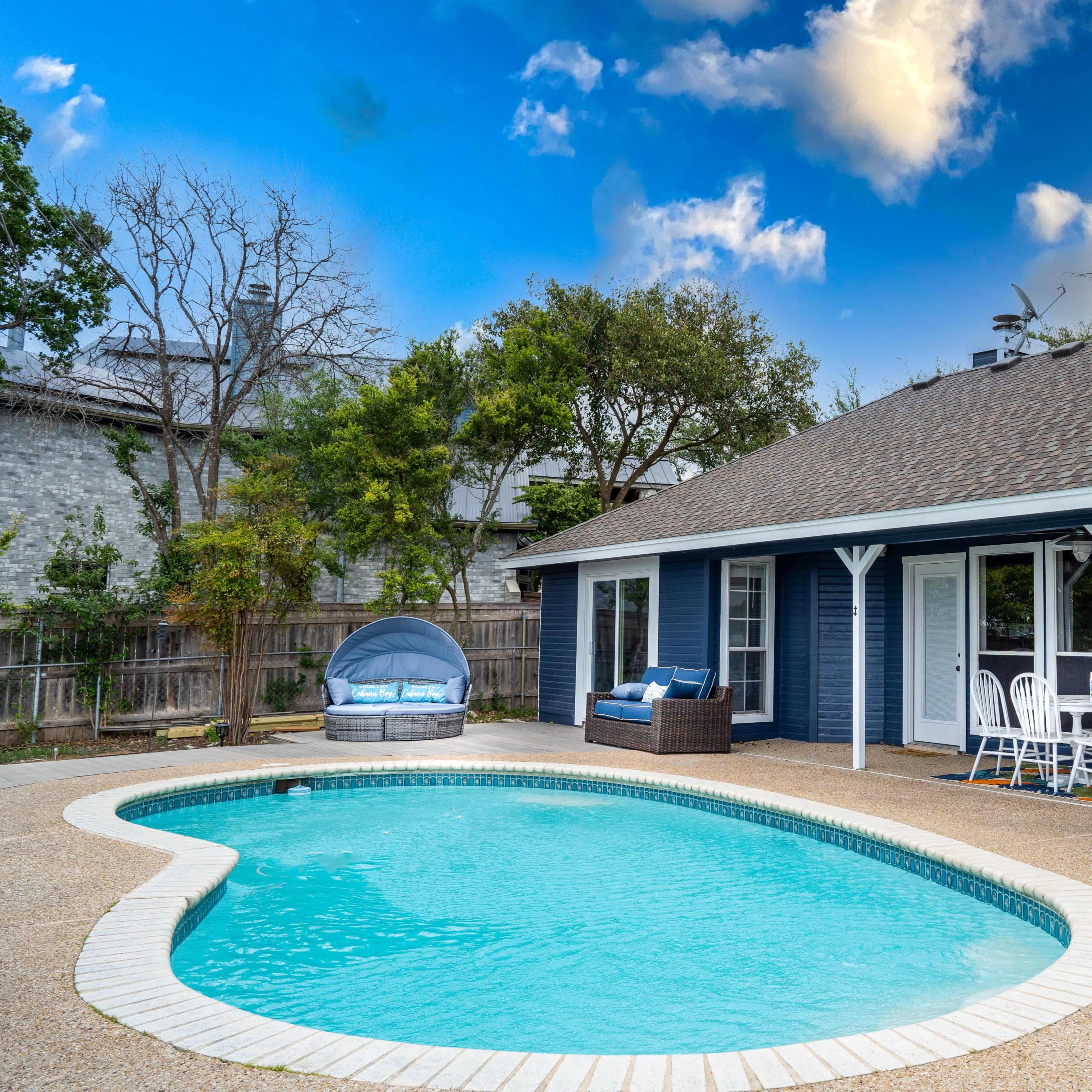 A residential patio area with a swimming pool, outdoor seating, and a clear blue sky.