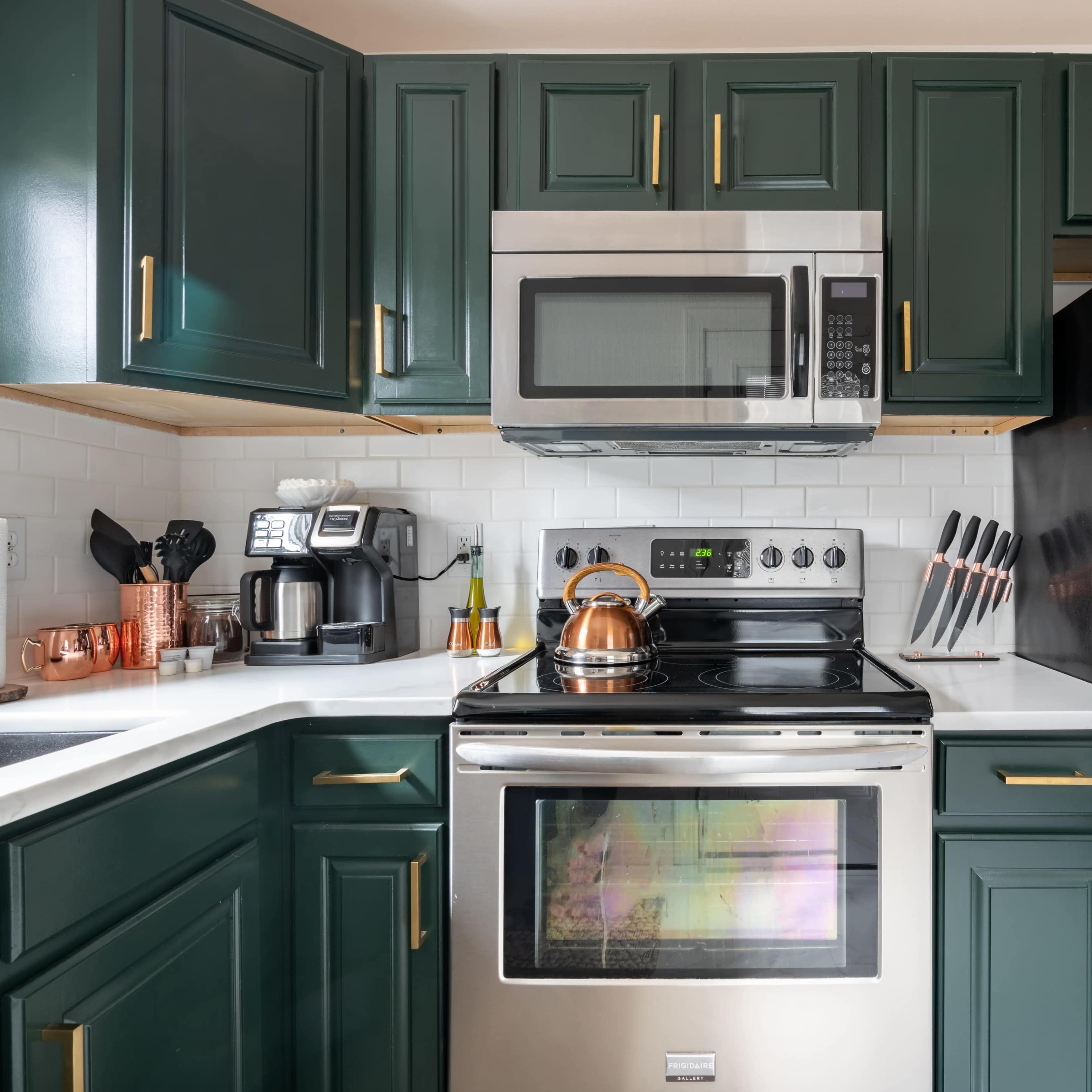 A kitchen features dark green cabinets, stainless steel appliances including a microwave and oven, and a black refrigerator.
