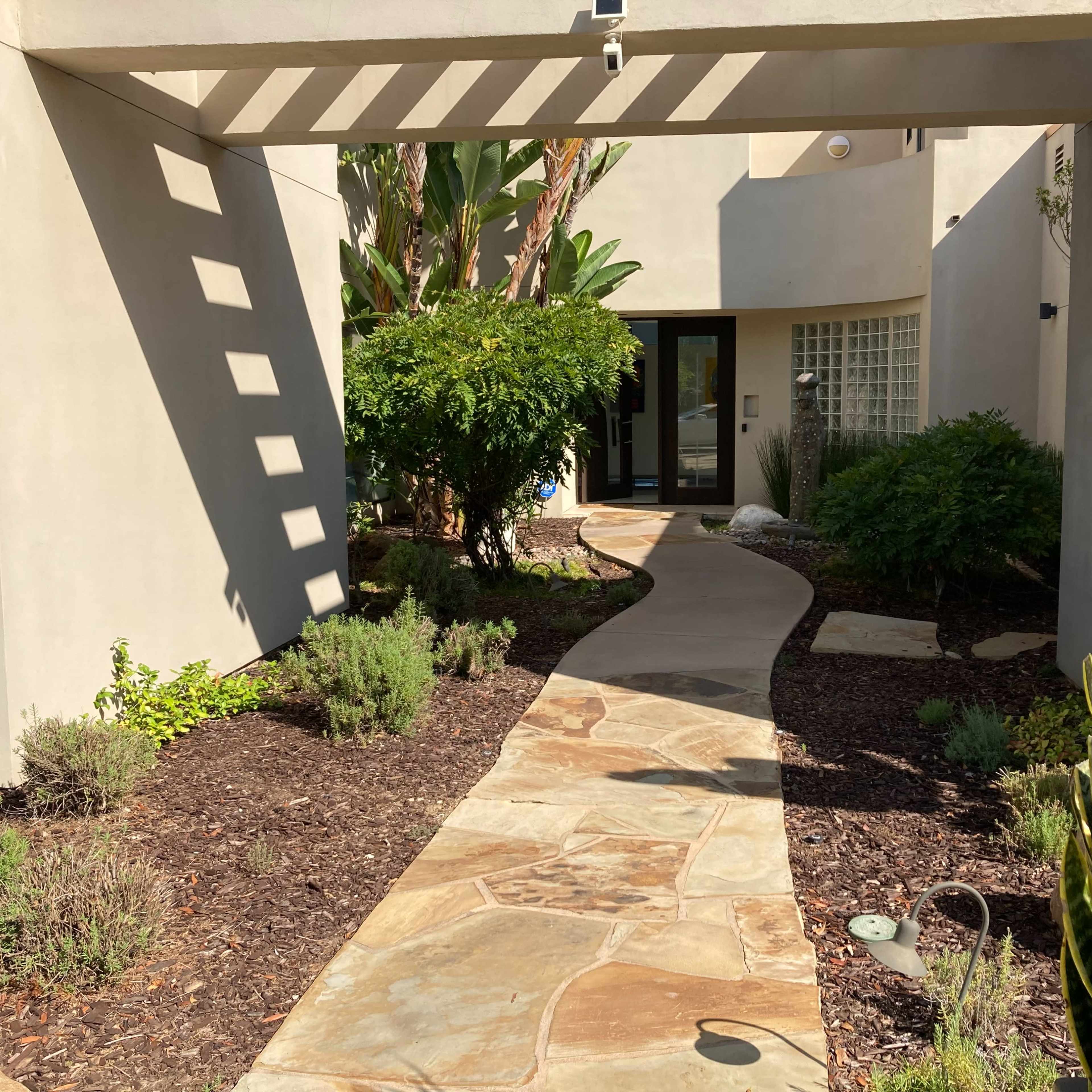 A stone path leads through a landscaped garden to the entrance of a modern building.