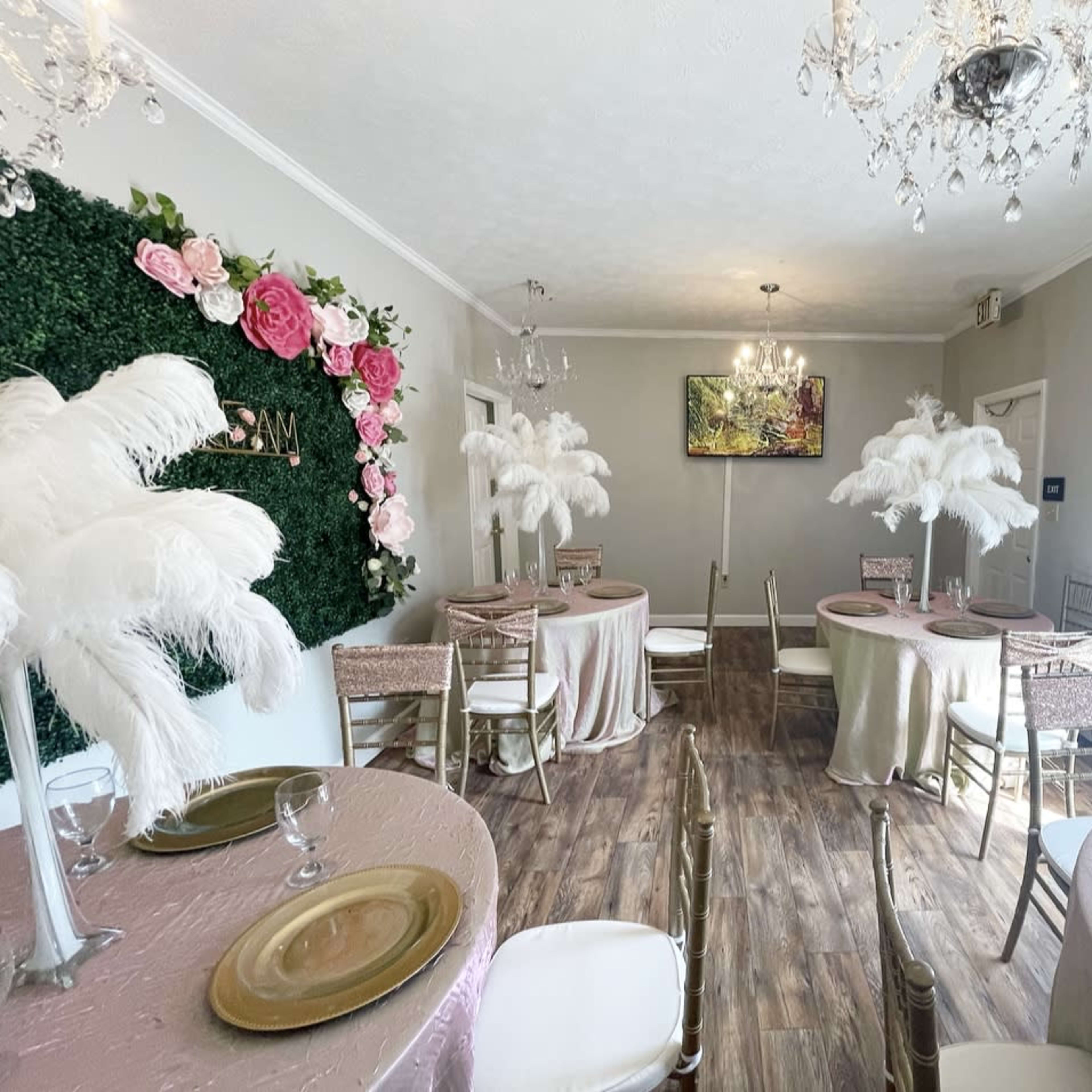 A stylishly decorated dining room with round tables covered in pastel tablecloths, adorned with feather centerpieces and floral wall accents.