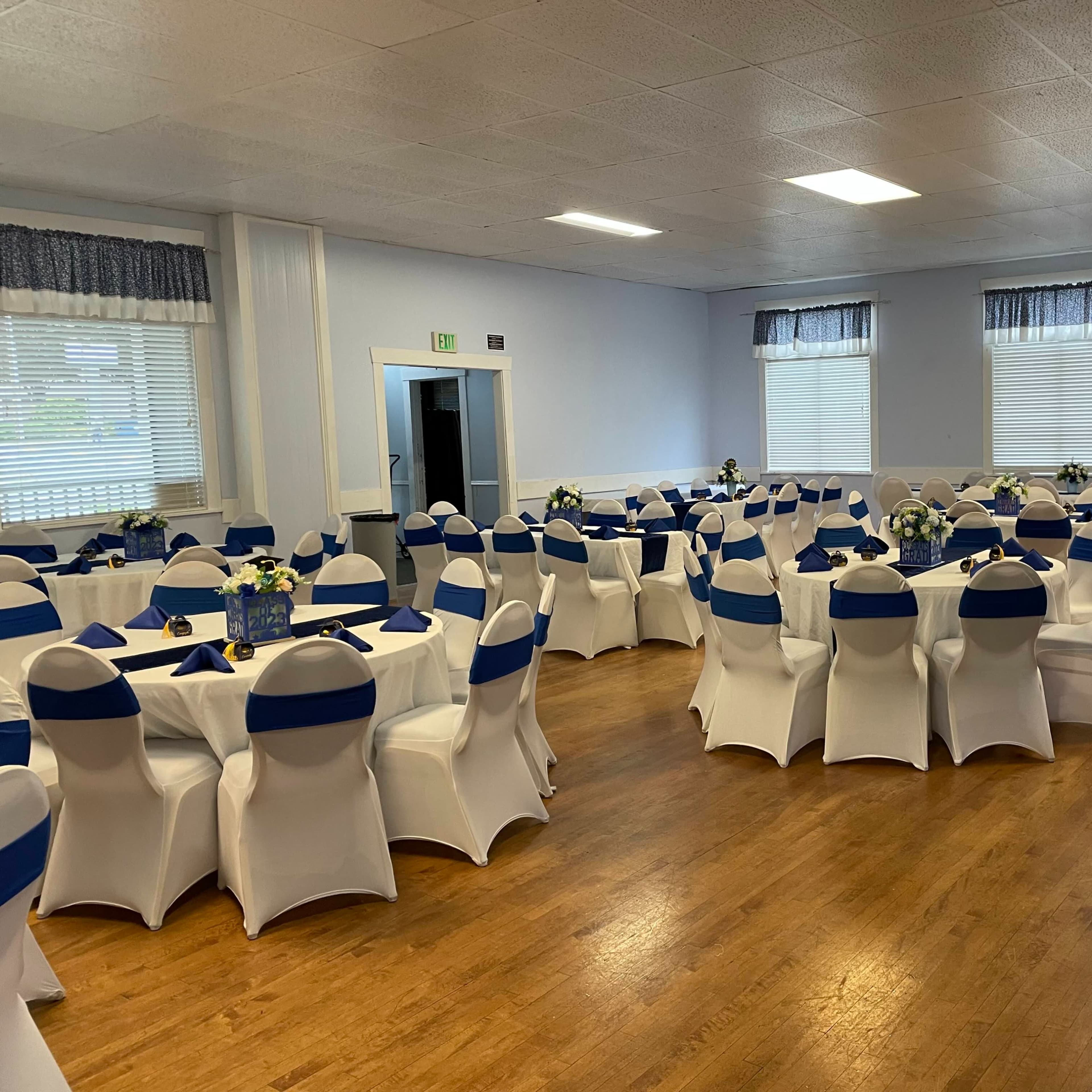 A banquet hall set up with round tables covered in white linens and blue chair sashes, arranged for an event.