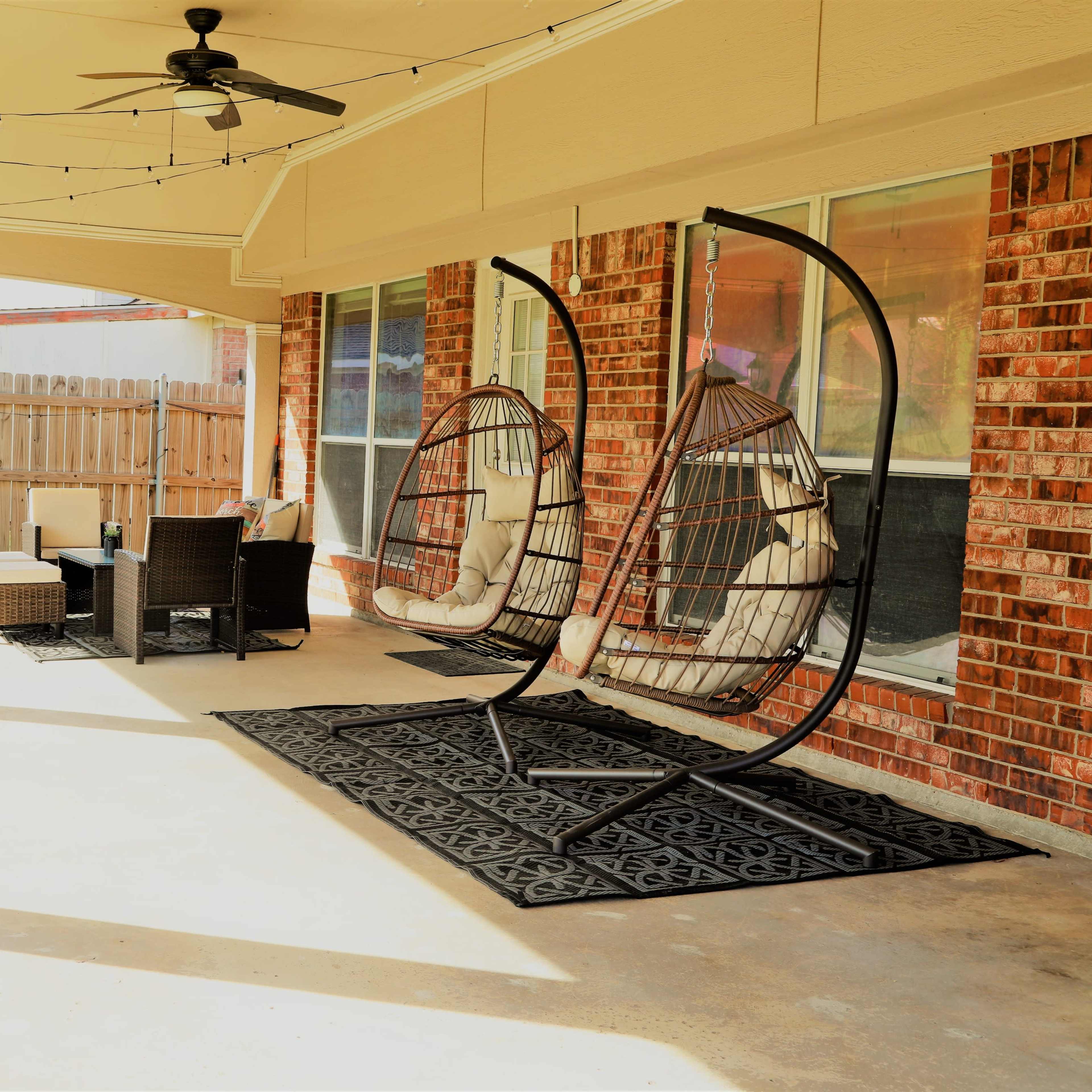 A covered patio with two hanging chairs, a small seating area with a table, and a wooden fence in the background.