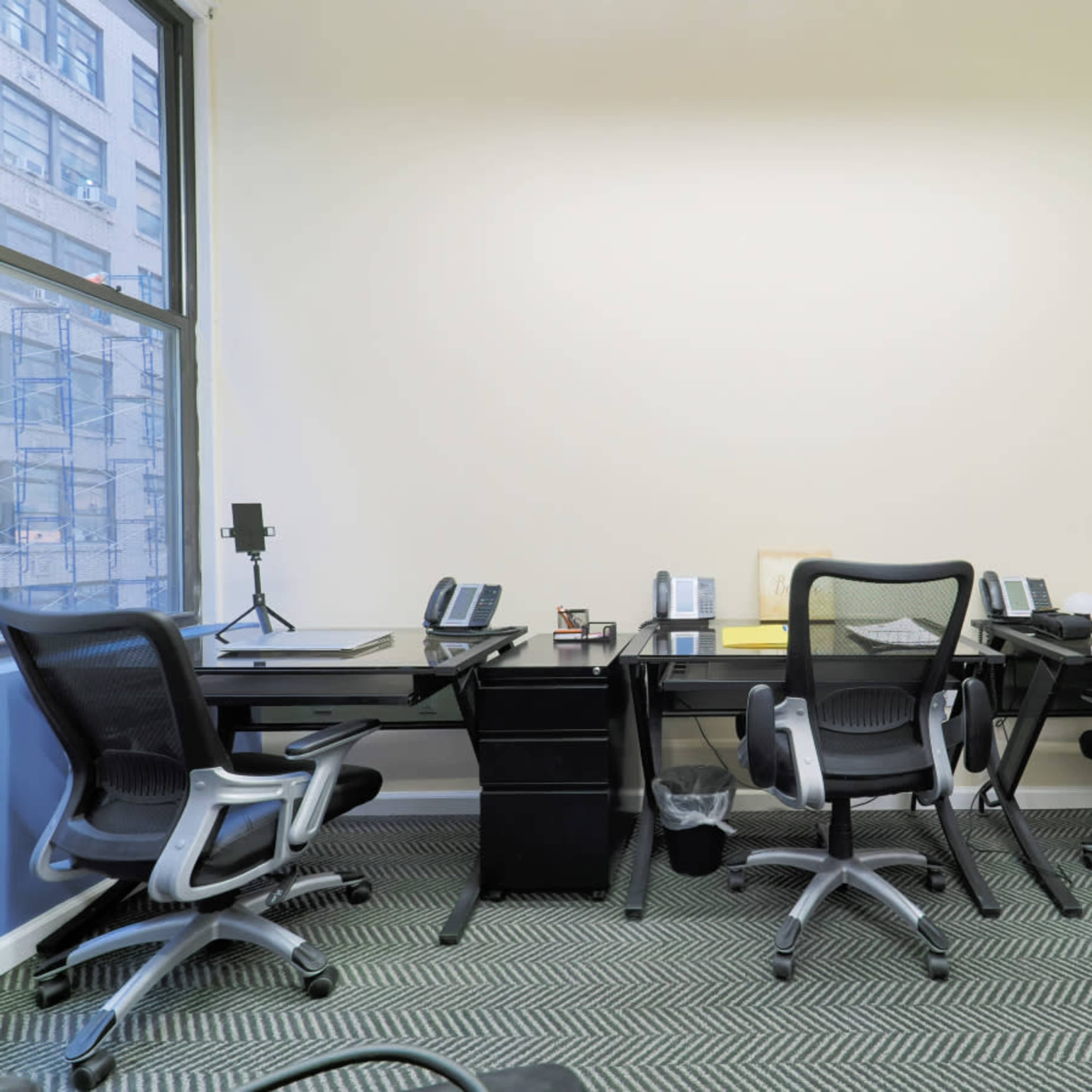 An office space with two desks, each equipped with telephones and other office supplies, surrounded by four office chairs.