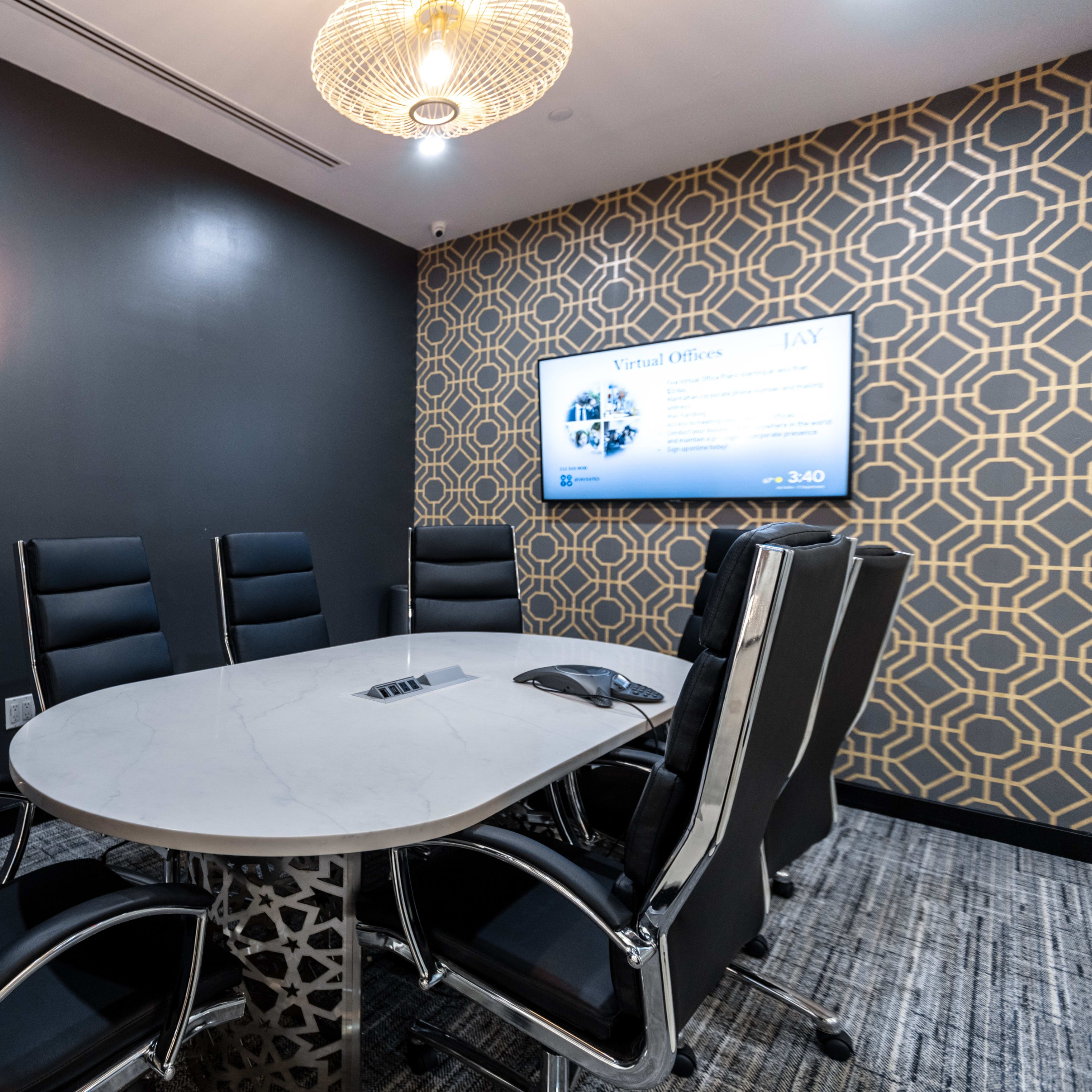 A modern conference room features a round table surrounded by ergonomic chairs, with a large screen displaying information on a patterned wall.