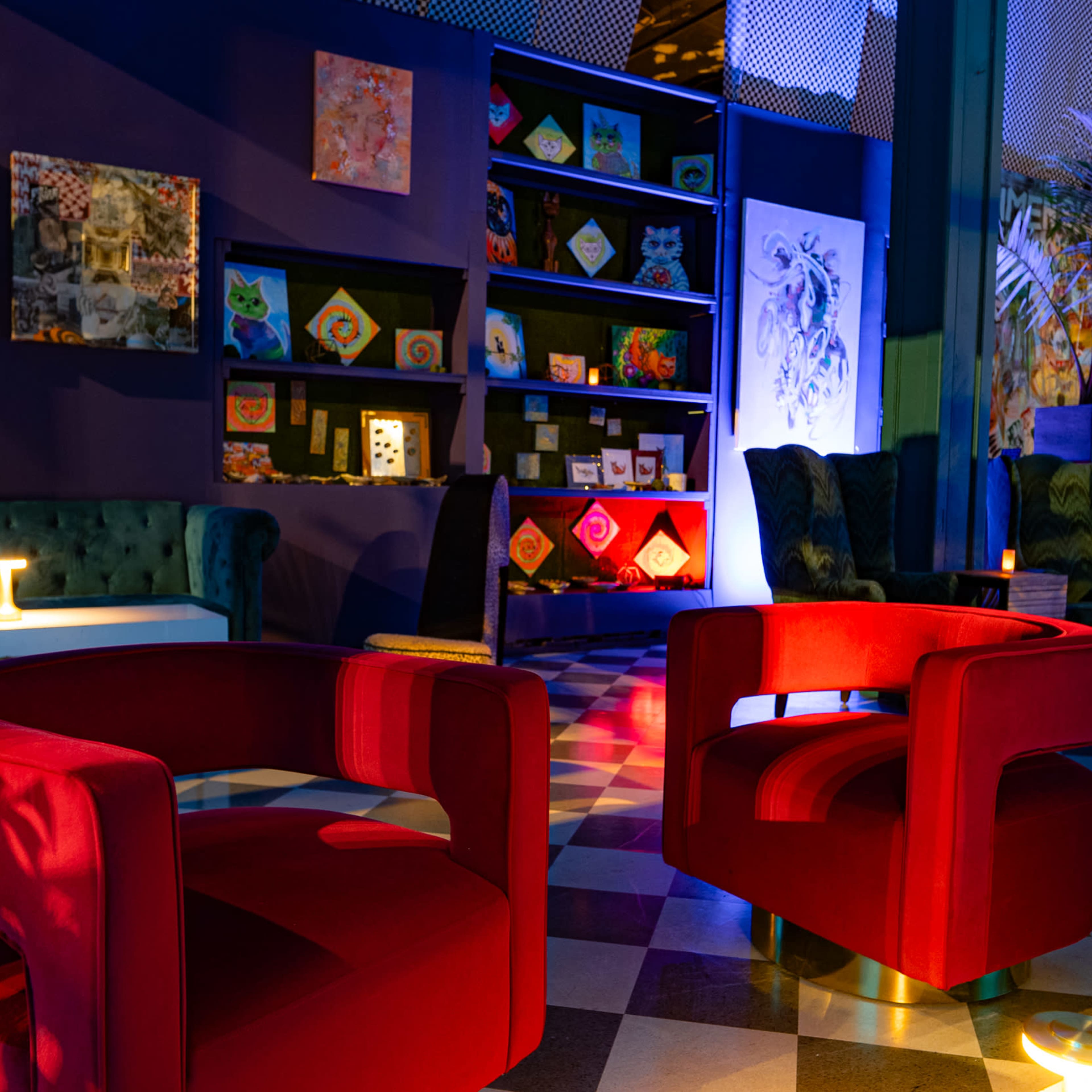 A lounge area with two red chairs, a coffee table, and a backdrop featuring colorful artwork on the walls.