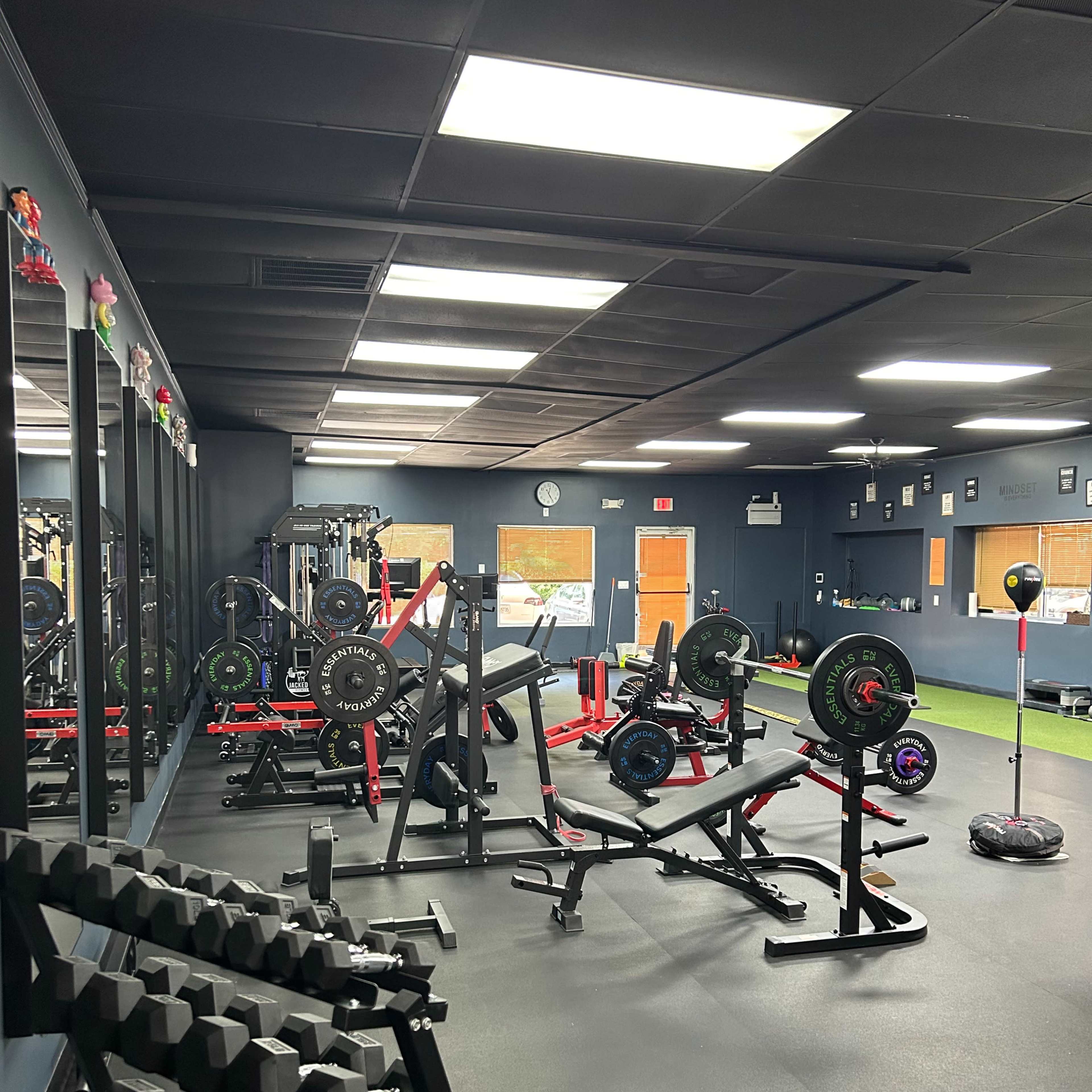 A gym interior with various weightlifting equipment, including benches, barbells, and dumbbells, arranged on a dark floor.