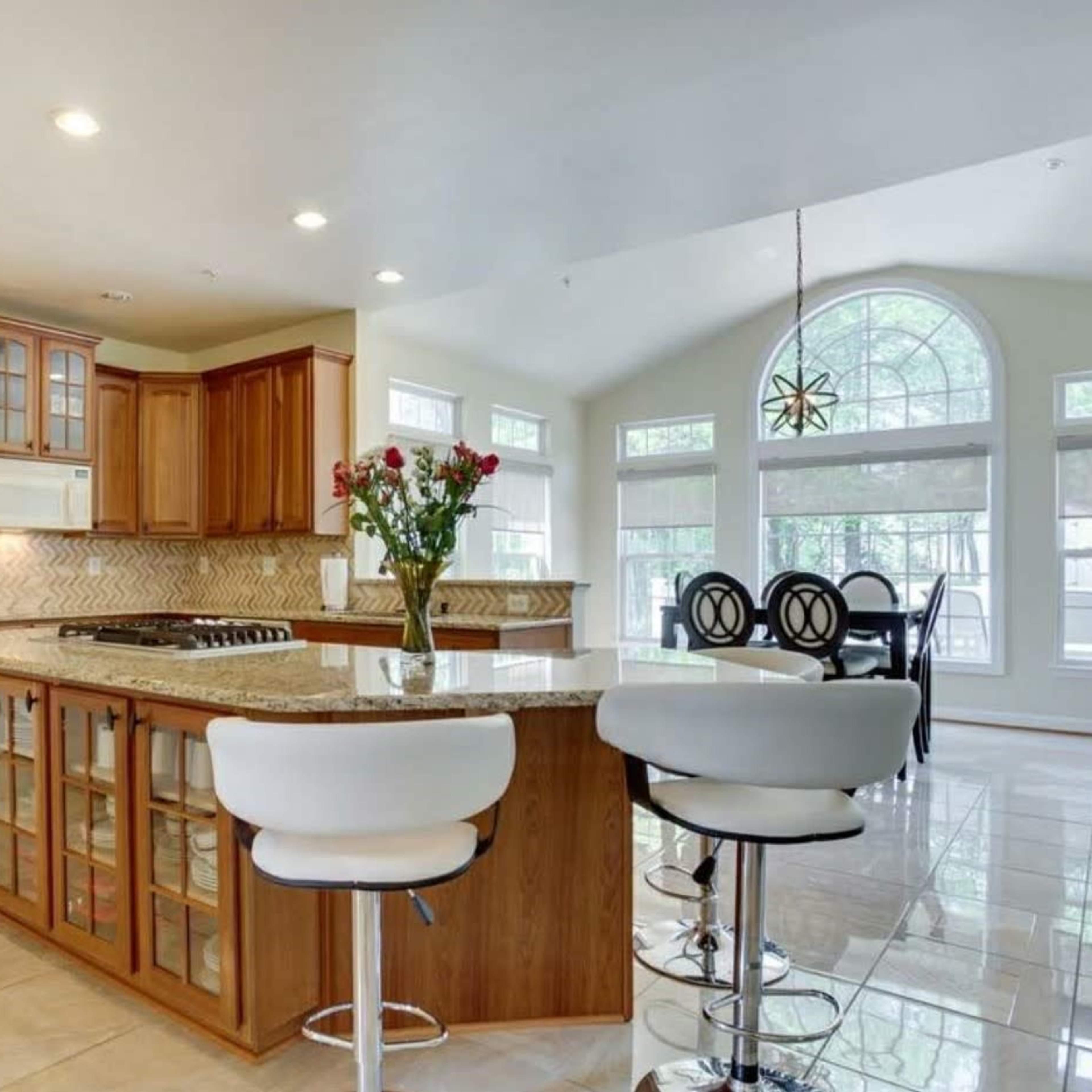 A modern kitchen with wooden cabinetry, a central island with bar stools, and large windows letting in natural light.