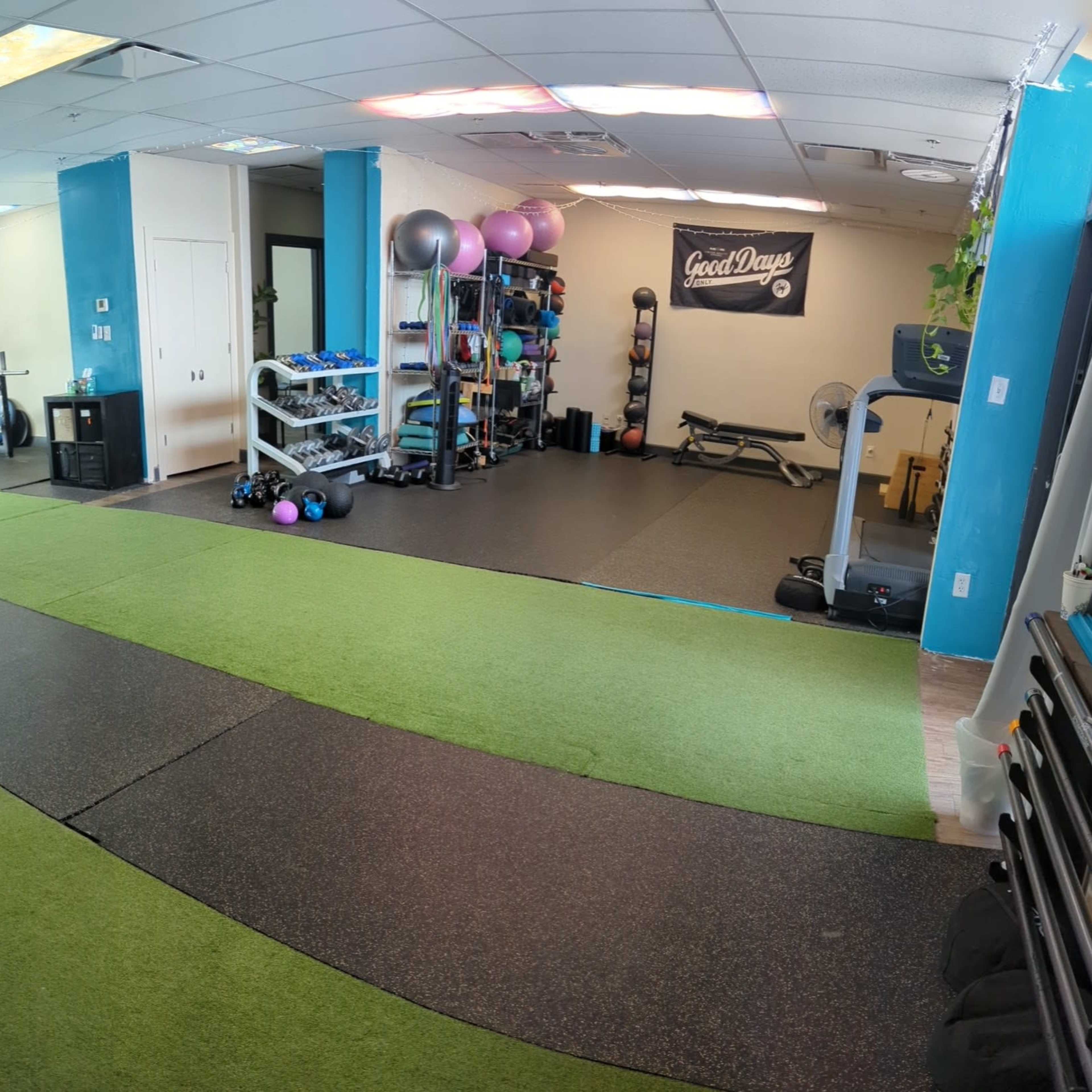 A gym interior featuring green turf flooring, various exercise equipment, and workout stations arranged in a spacious layout.