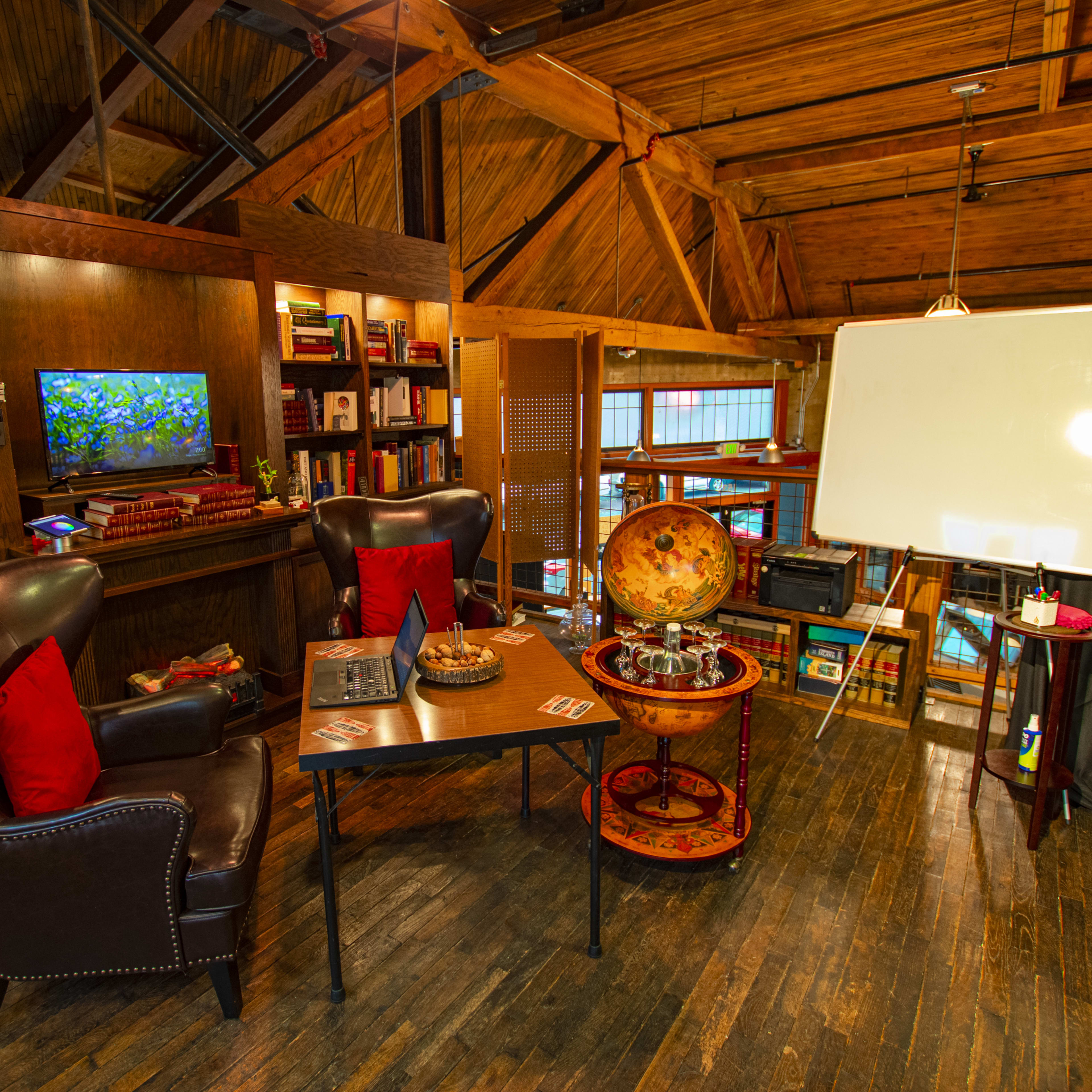 A cozy, wooden-paneled room with two armchairs, a table, a globe, a whiteboard, and bookshelves filled with books.