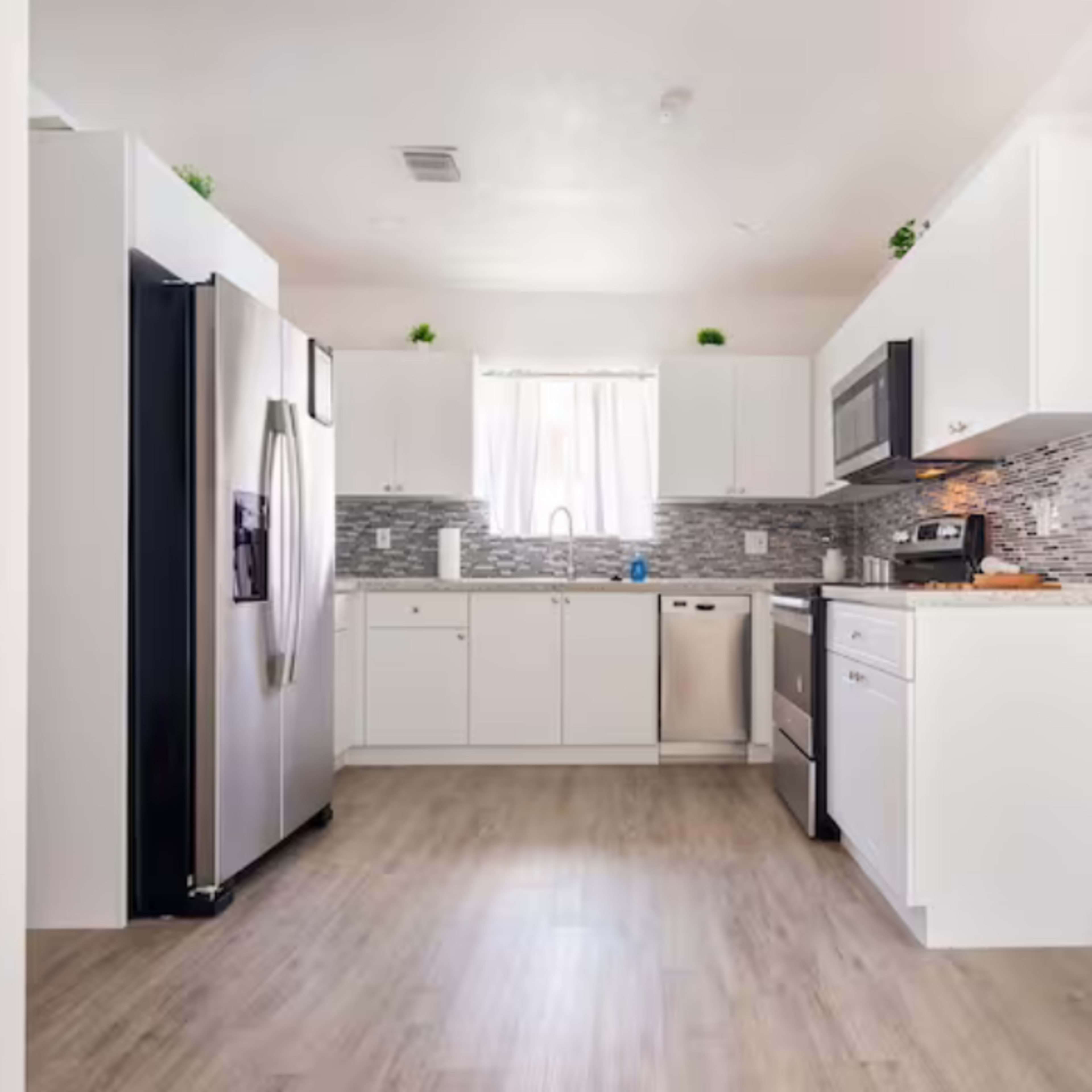 The kitchen features stainless steel appliances, white cabinets, and a mosaic tiled backsplash.