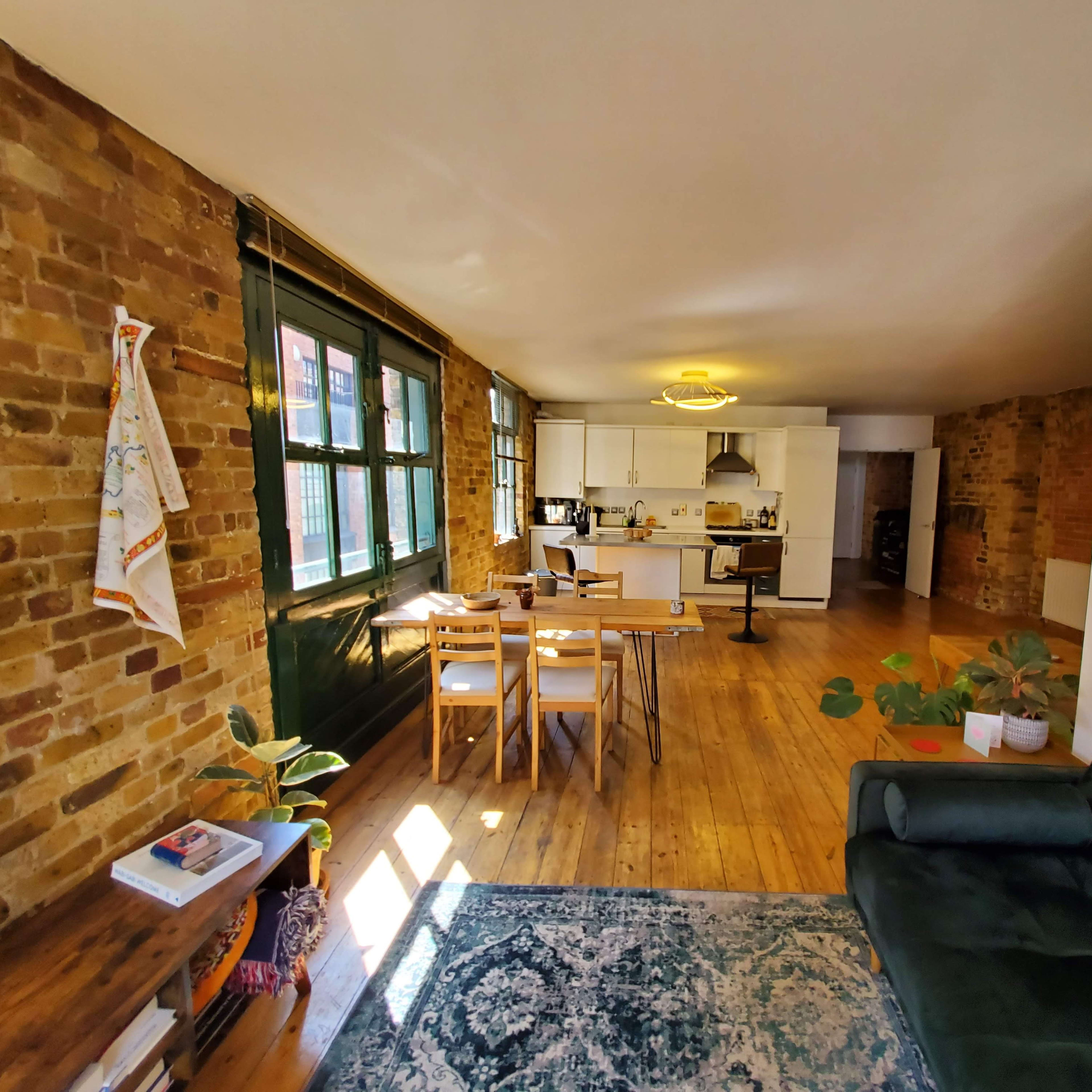 A spacious, open-concept living area featuring exposed brick walls, a dining table, and a kitchen at the far end.