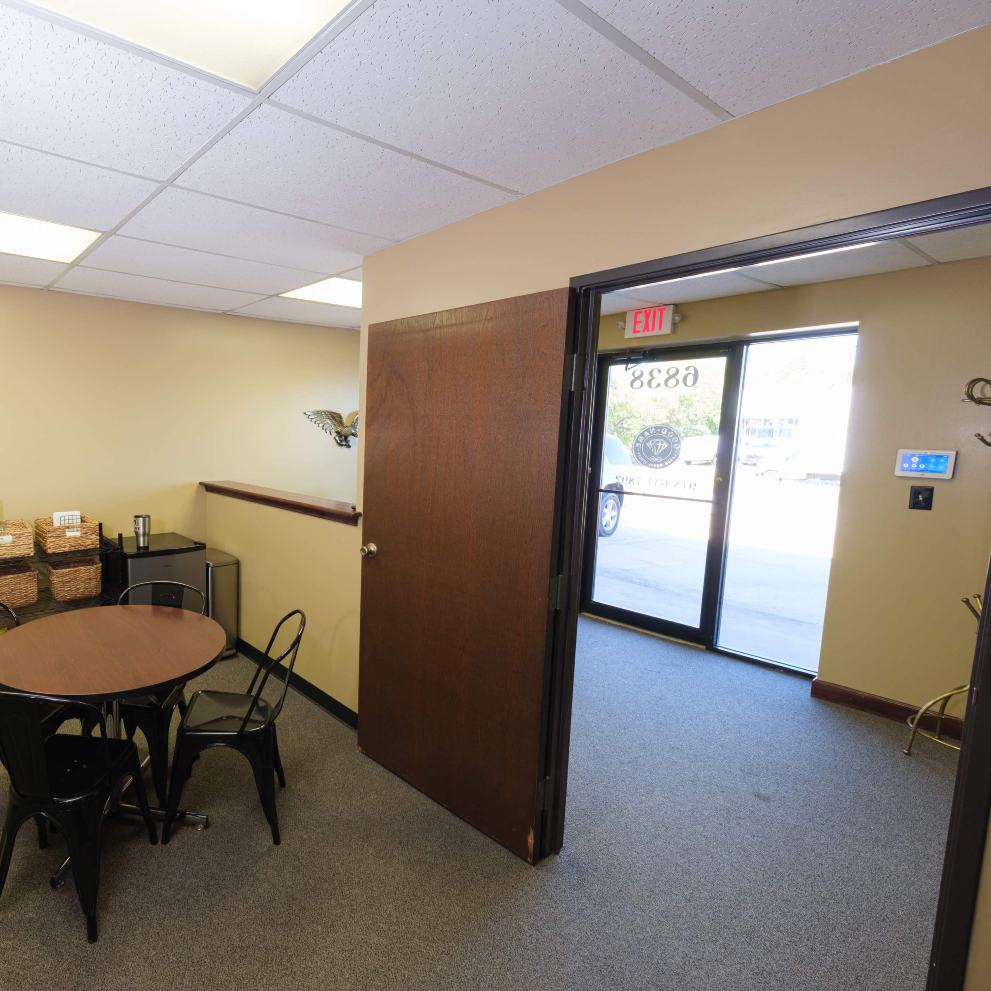 A small interior room with a circular table and four black chairs, a beverage station, and a doorway leading outside.