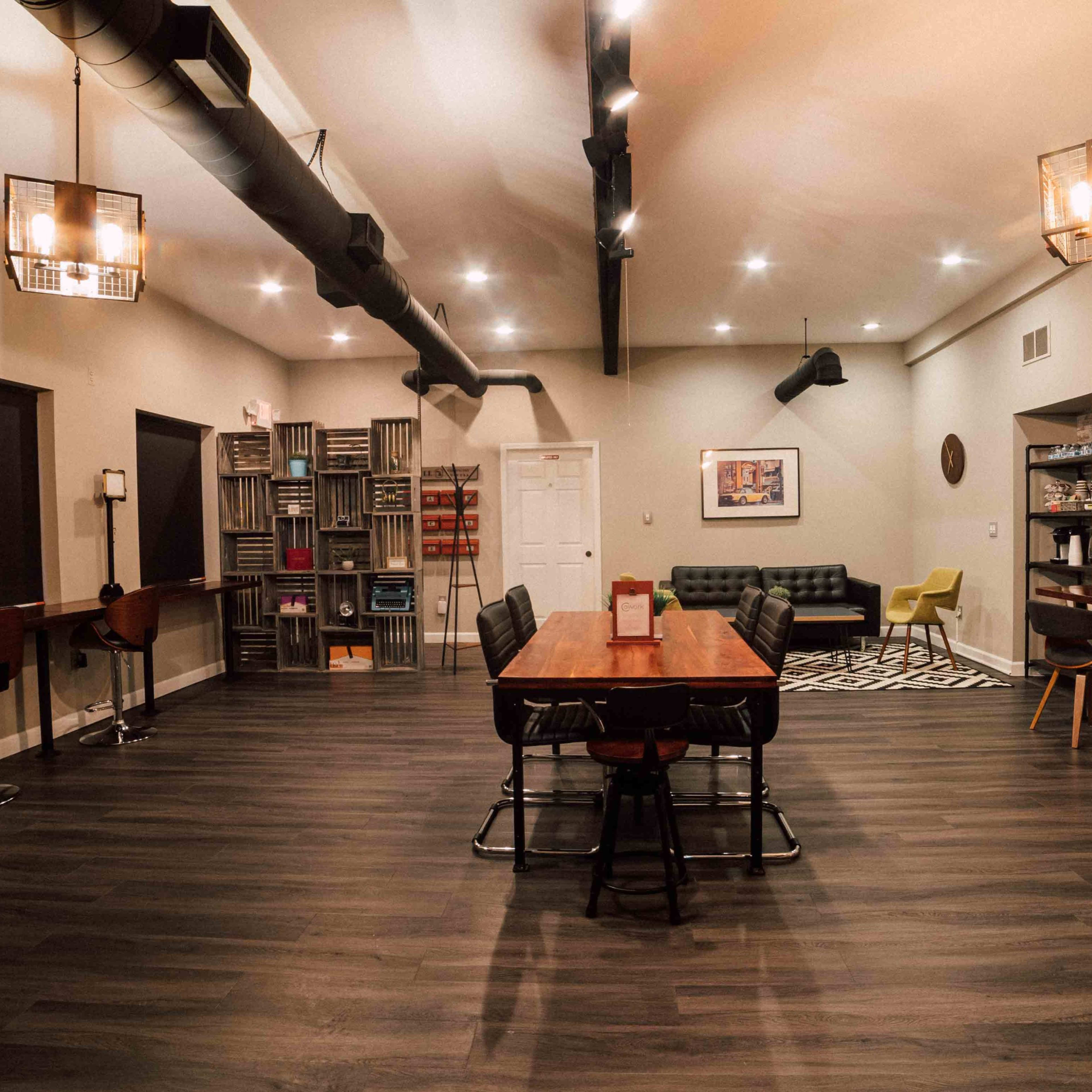 A spacious, modern room with wooden floors, several seating areas, and a long dining table in the center.