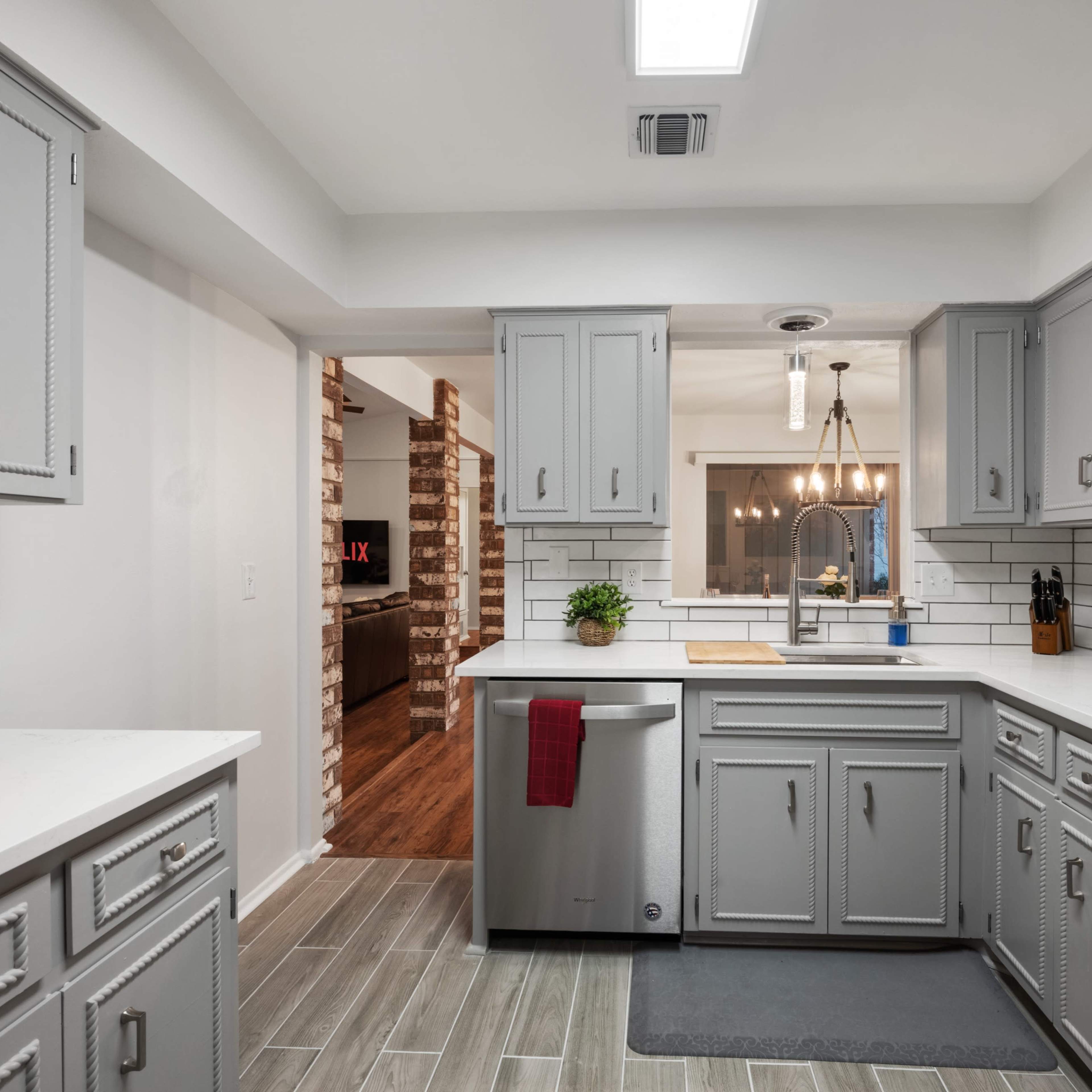 A modern kitchen with gray cabinets, a stainless steel dishwasher, white countertops, and patterned tile flooring.