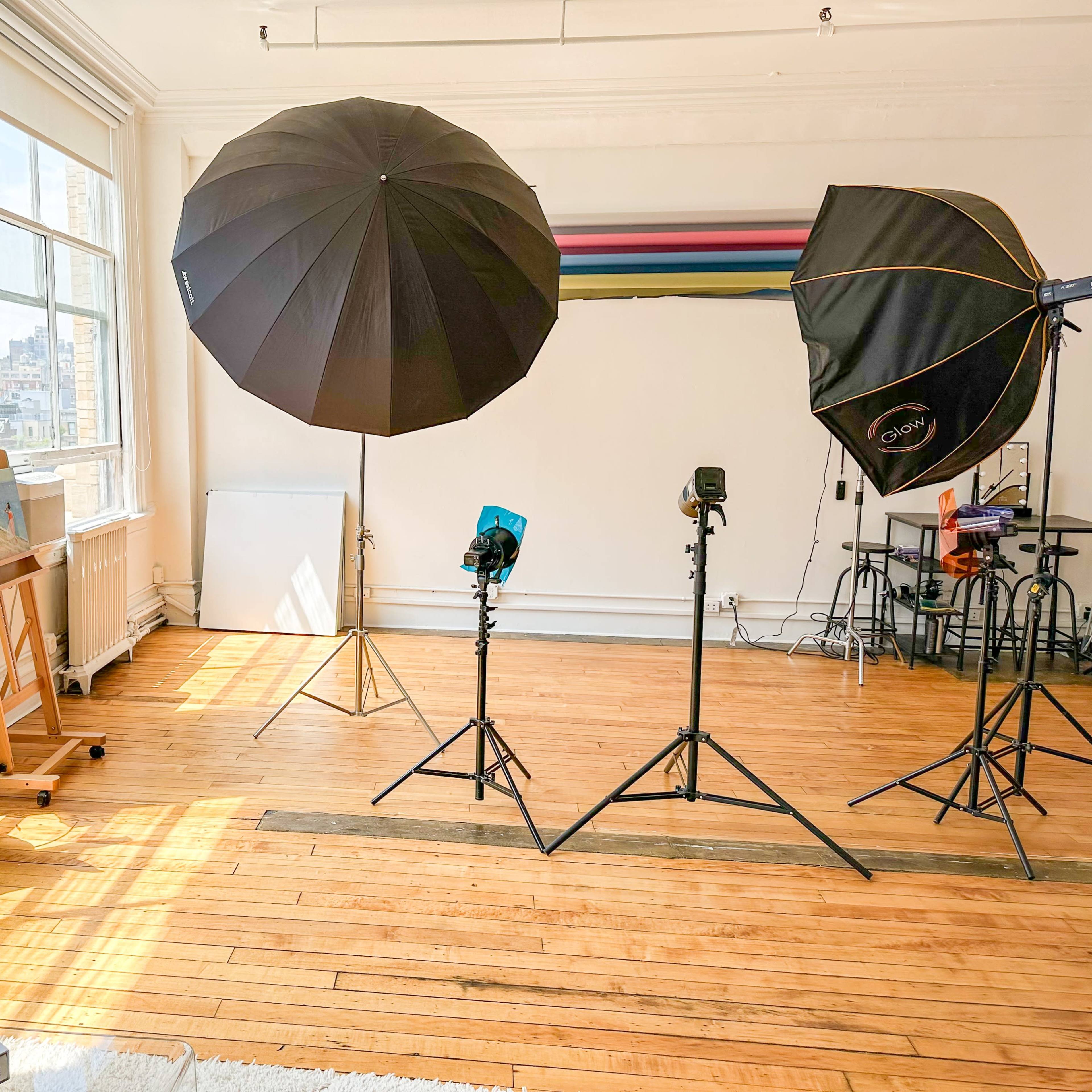 A bright photography studio with large softbox lights, an easel, and wooden floors.