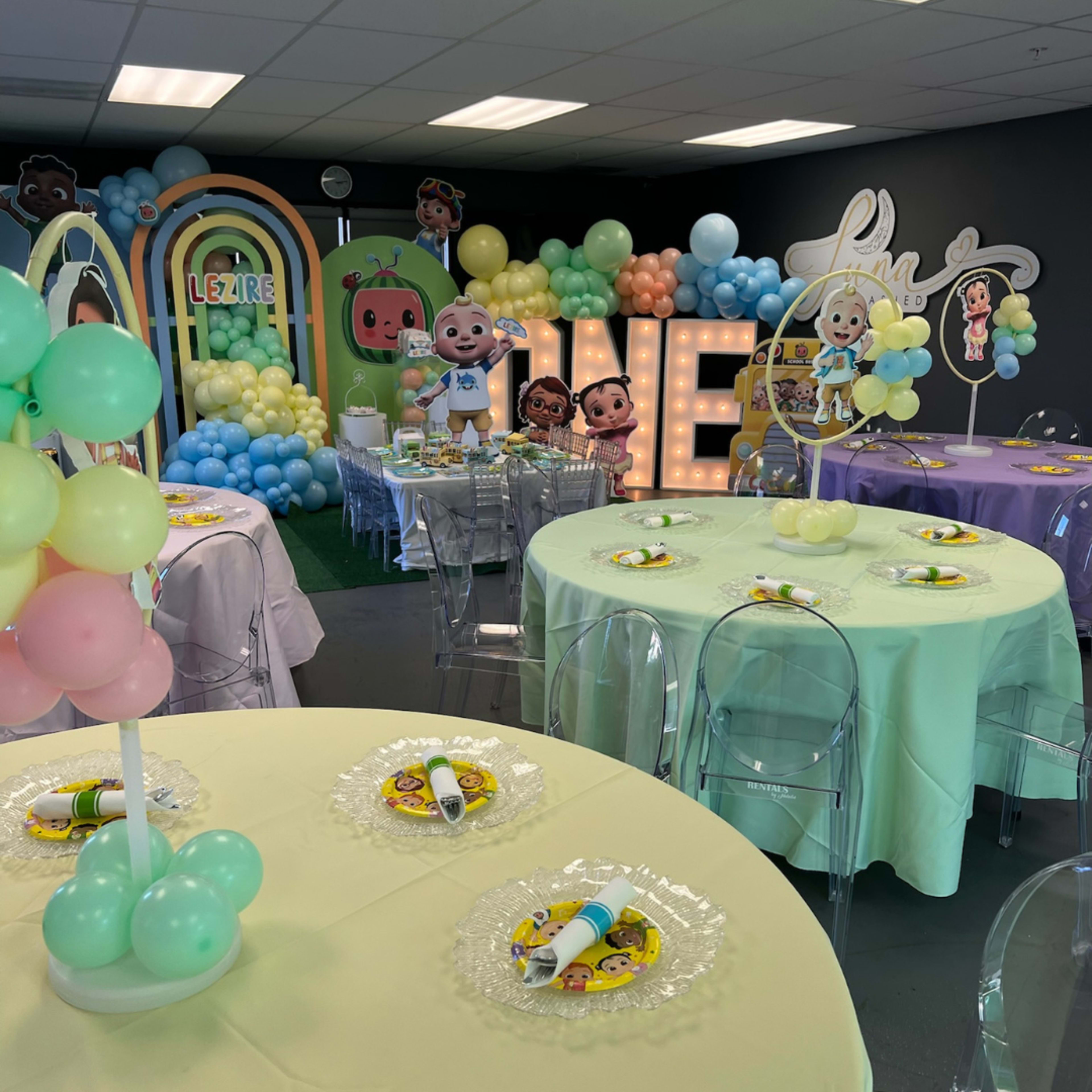 A decorated party space with colorful balloon arrangements, themed table settings, and character cutouts in the background.