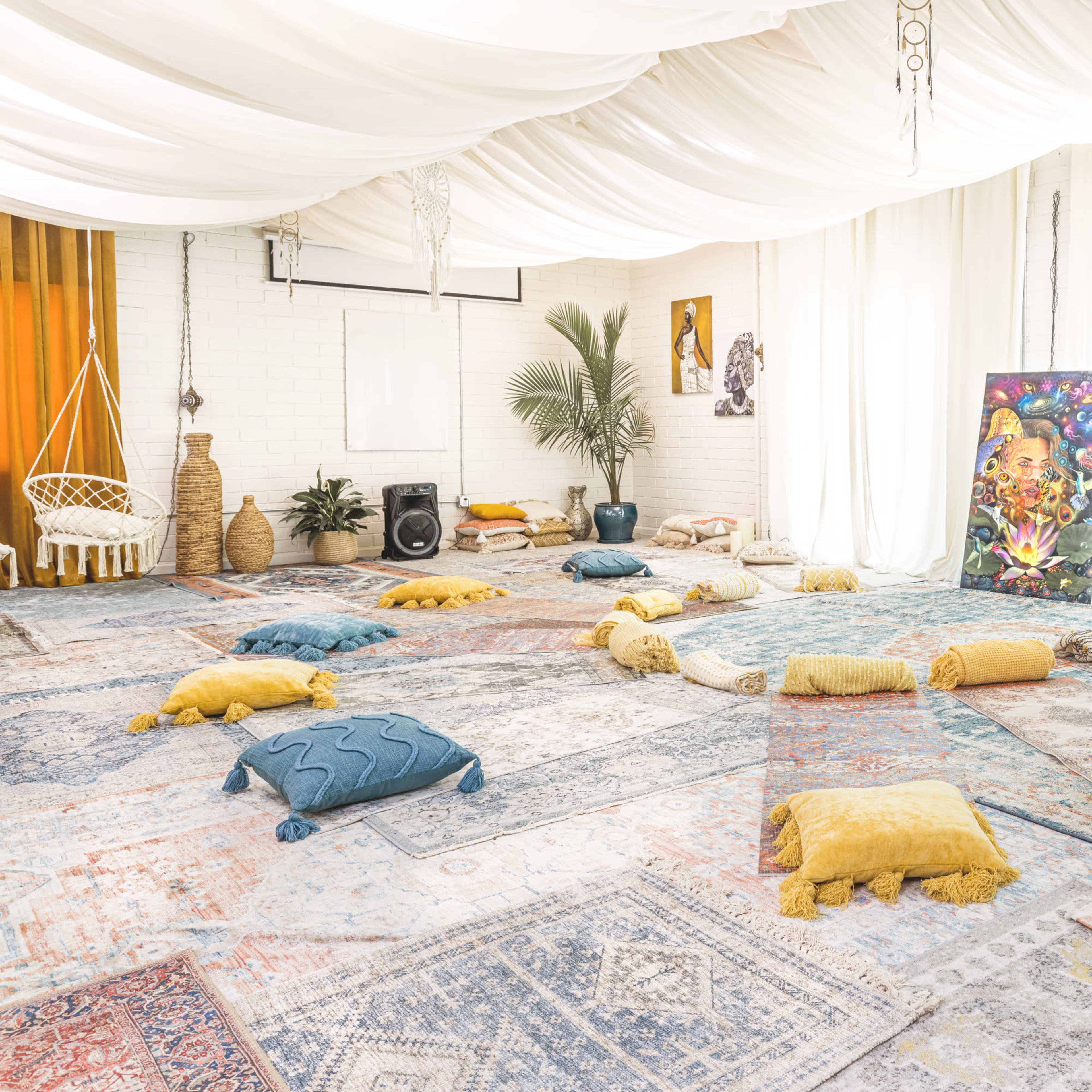 A spacious room decorated with vibrant rugs, floor cushions, and a large colorful artwork, all under a draped ceiling.