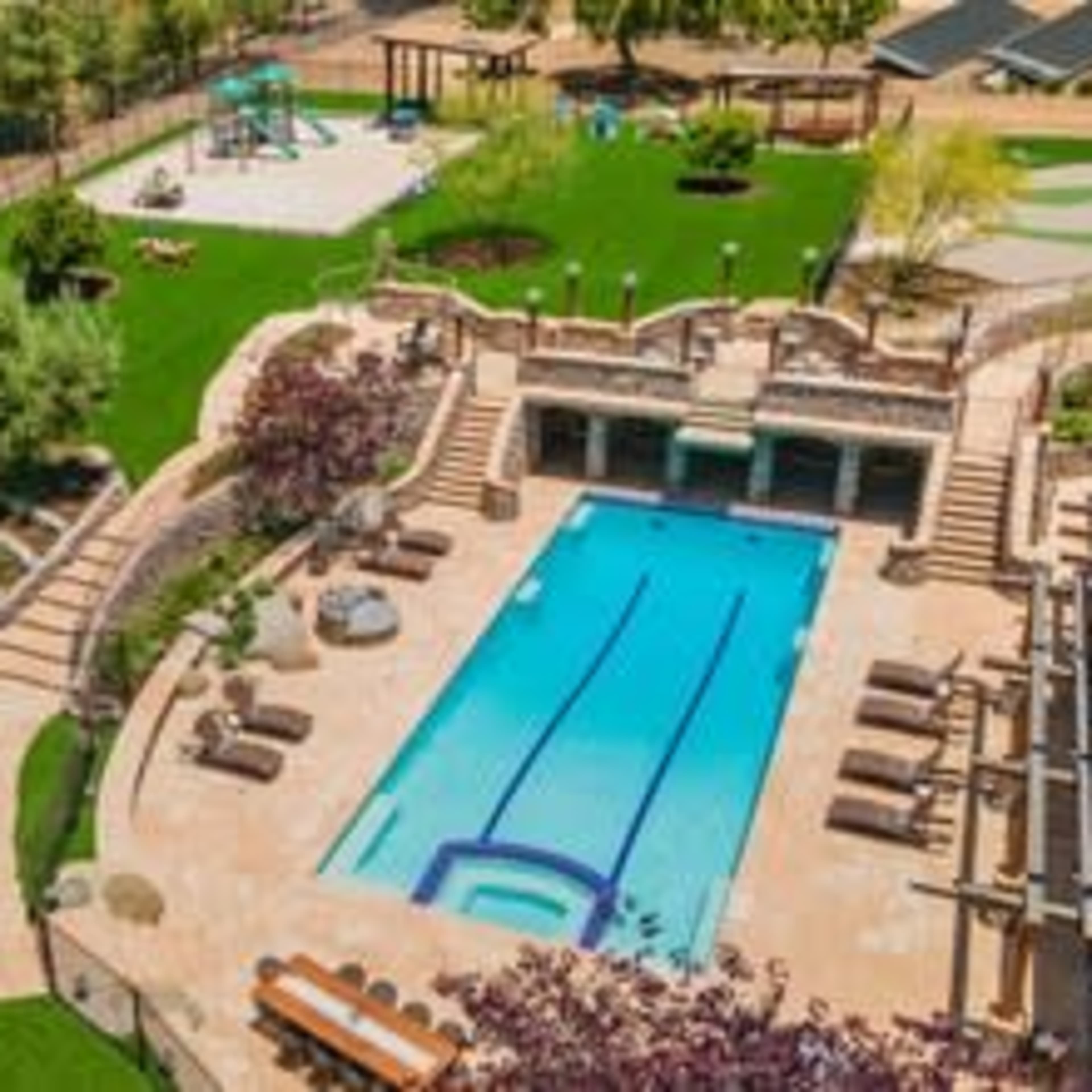 A well-designed outdoor area featuring a swimming pool, landscaped gardens, a playground, and various seating spaces.