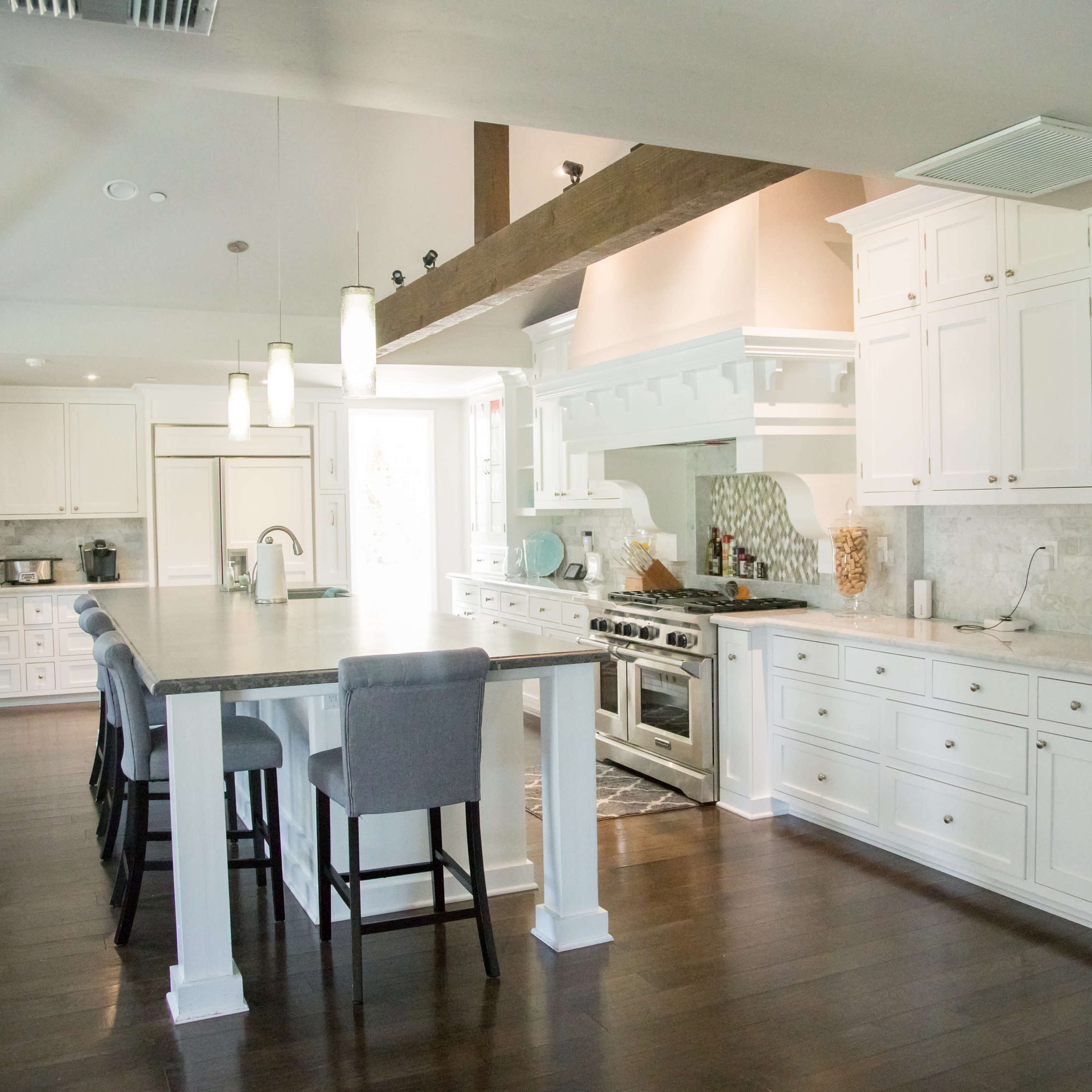 The kitchen features white cabinetry, a large island with bar seating, stainless steel appliances, and a spacious layout with hardwood flooring.