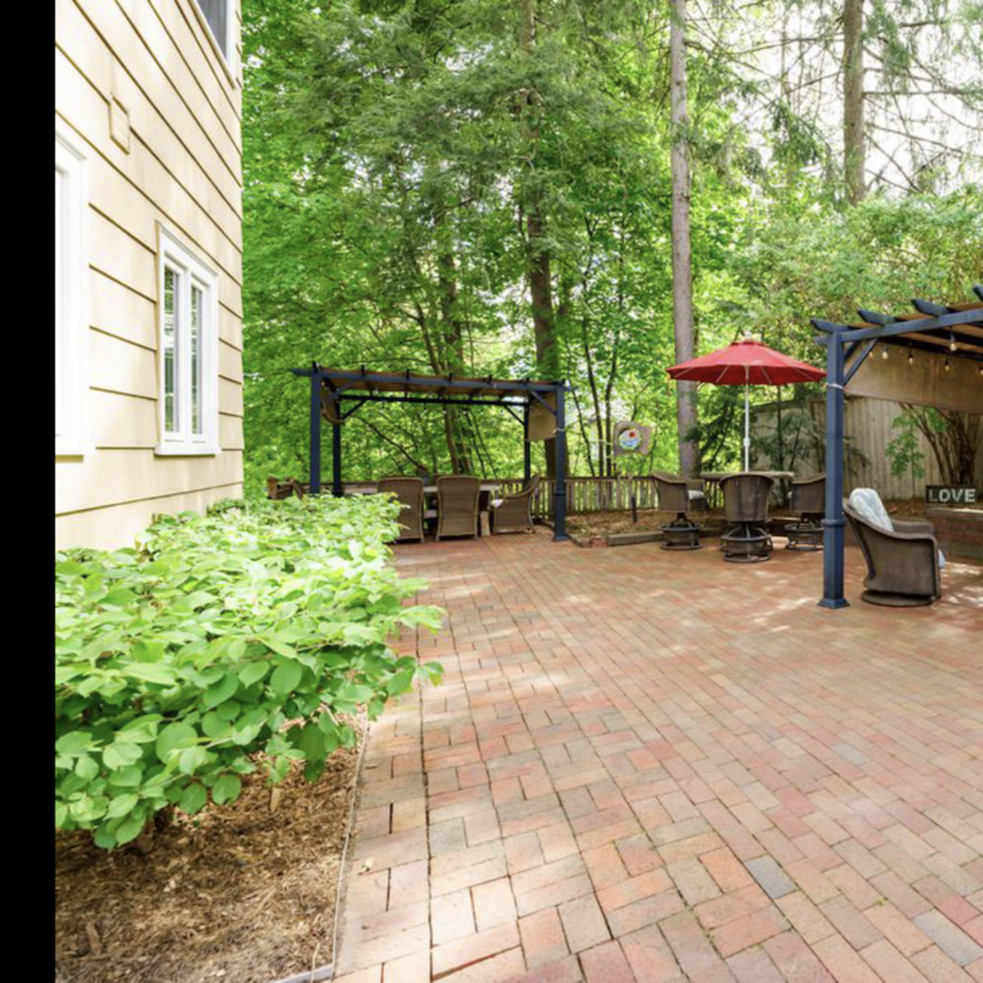 A brick patio with seating areas covered by pergolas surrounded by greenery.