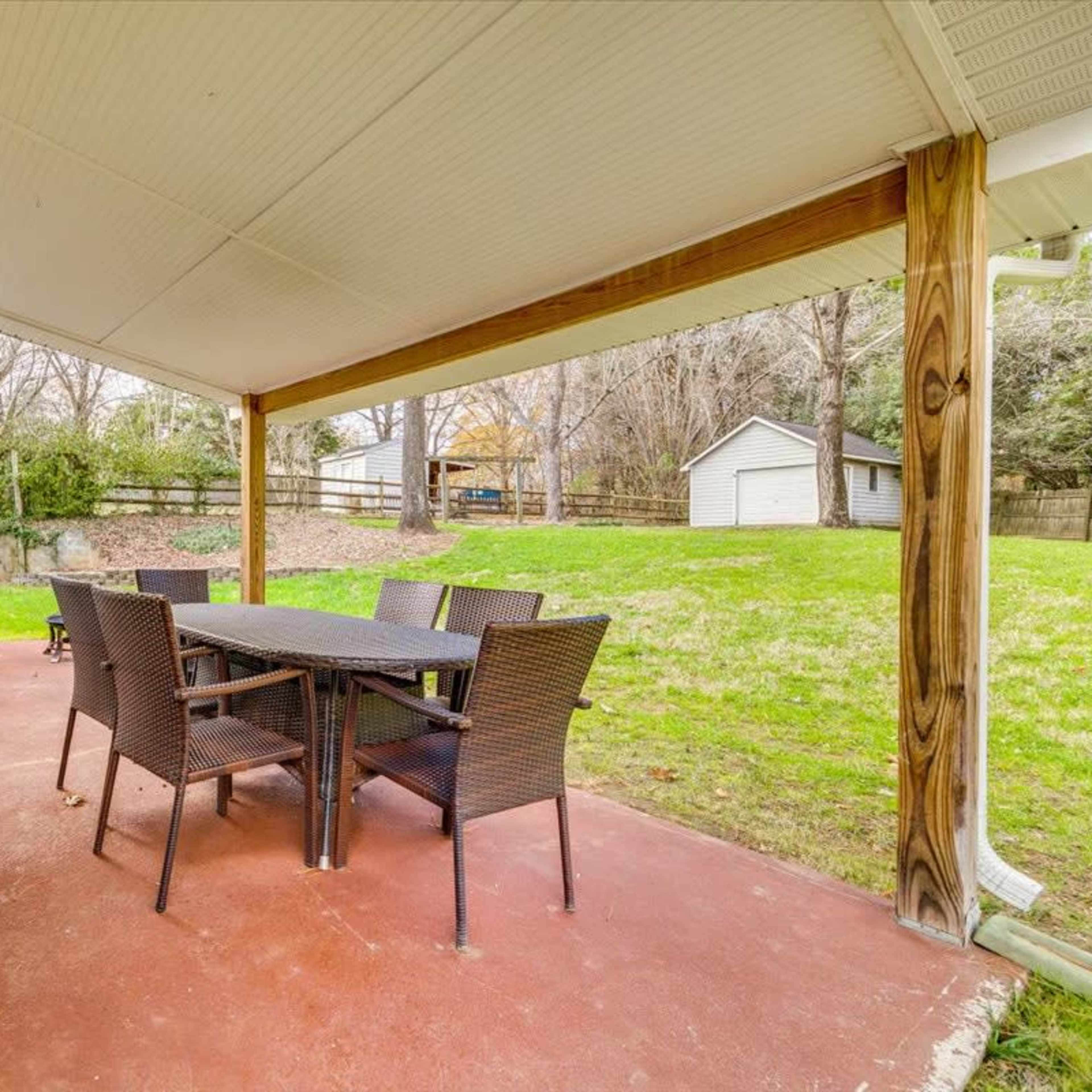 A covered outdoor patio with a table and six chairs, adjacent to a grassy backyard and a shed in the background.