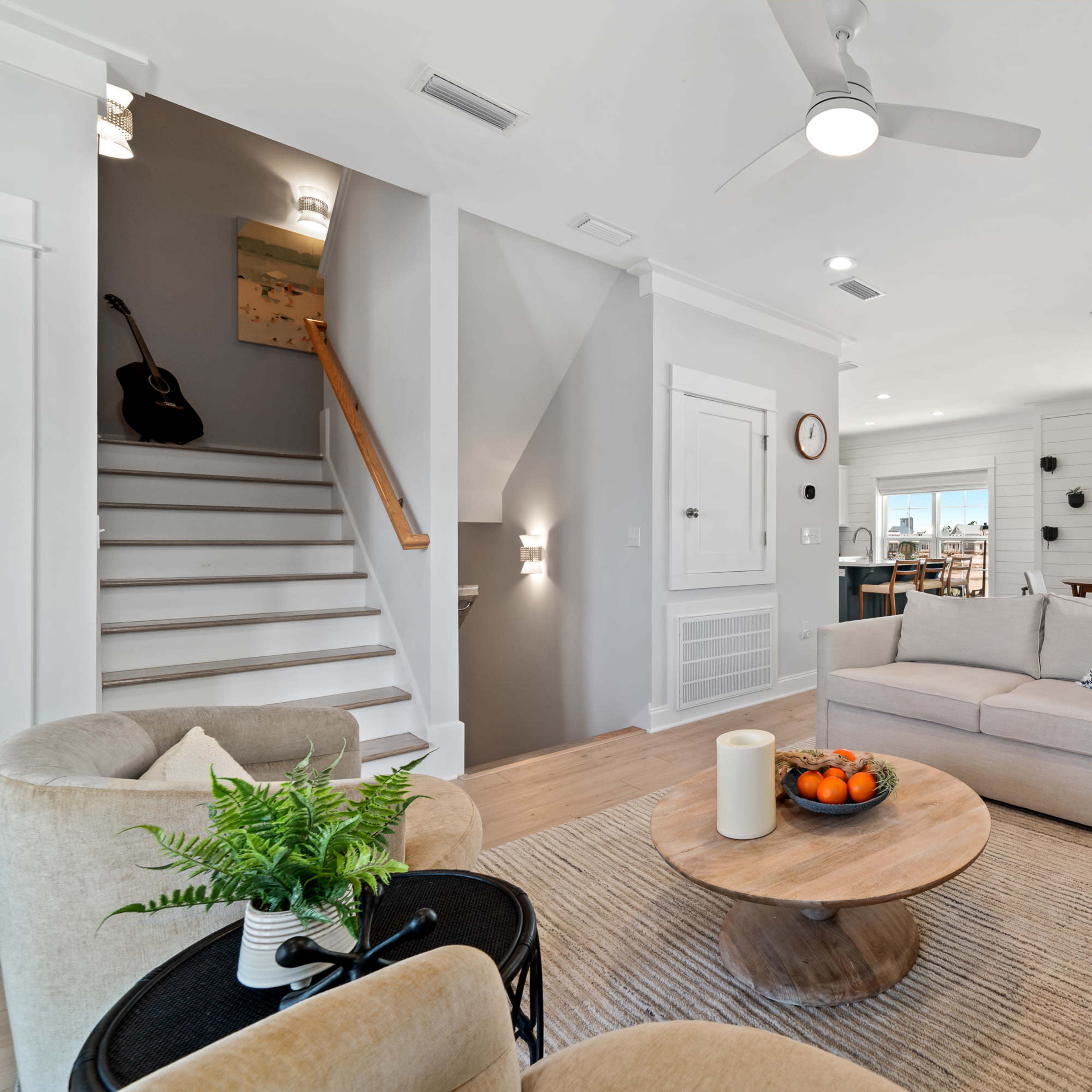 The living space features a light-filled area with a sofa, coffee table, and plants, alongside a staircase leading to the upper floor.