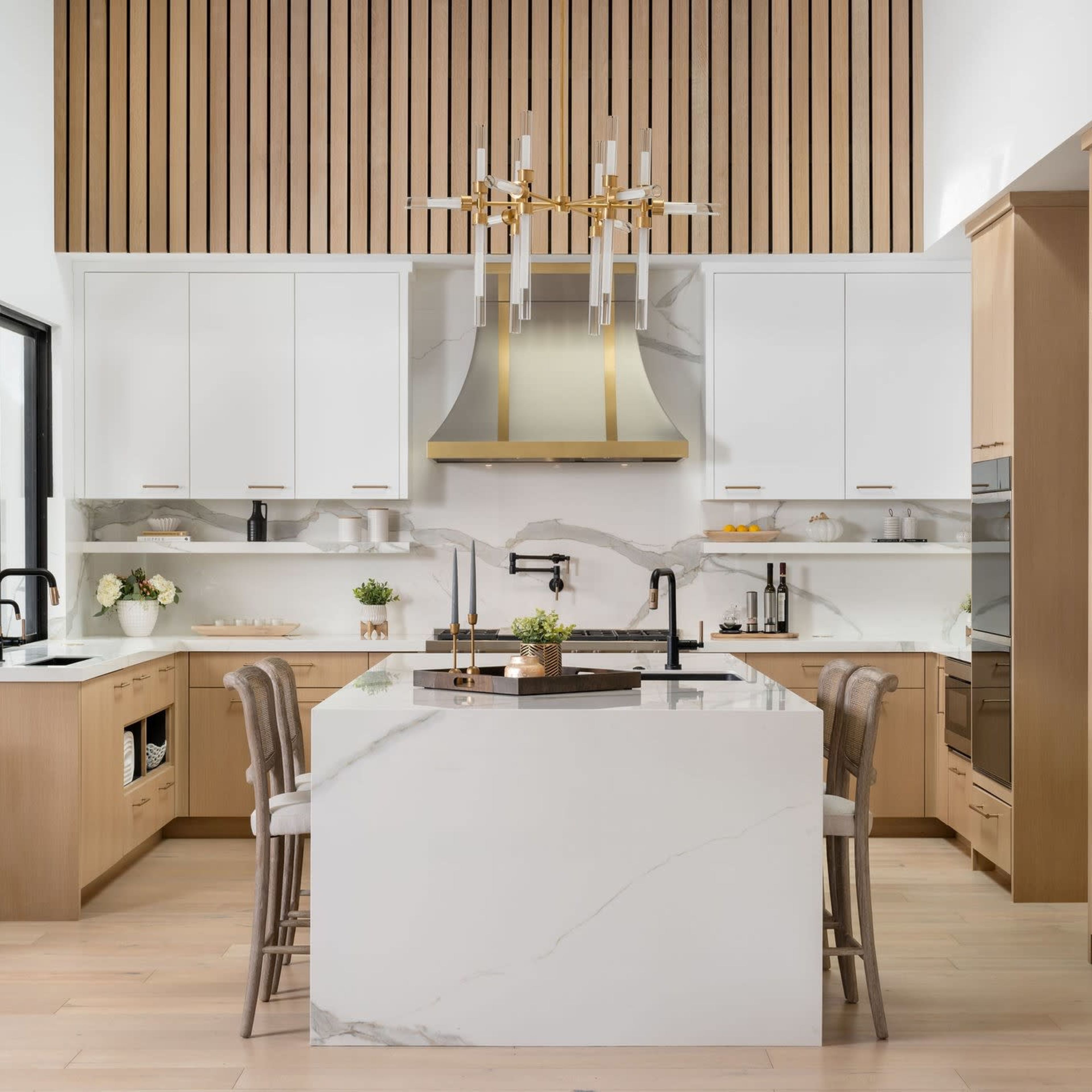 The kitchen features a large island with a marble countertop, wooden cabinetry, and modern appliances under a stylish light fixture.