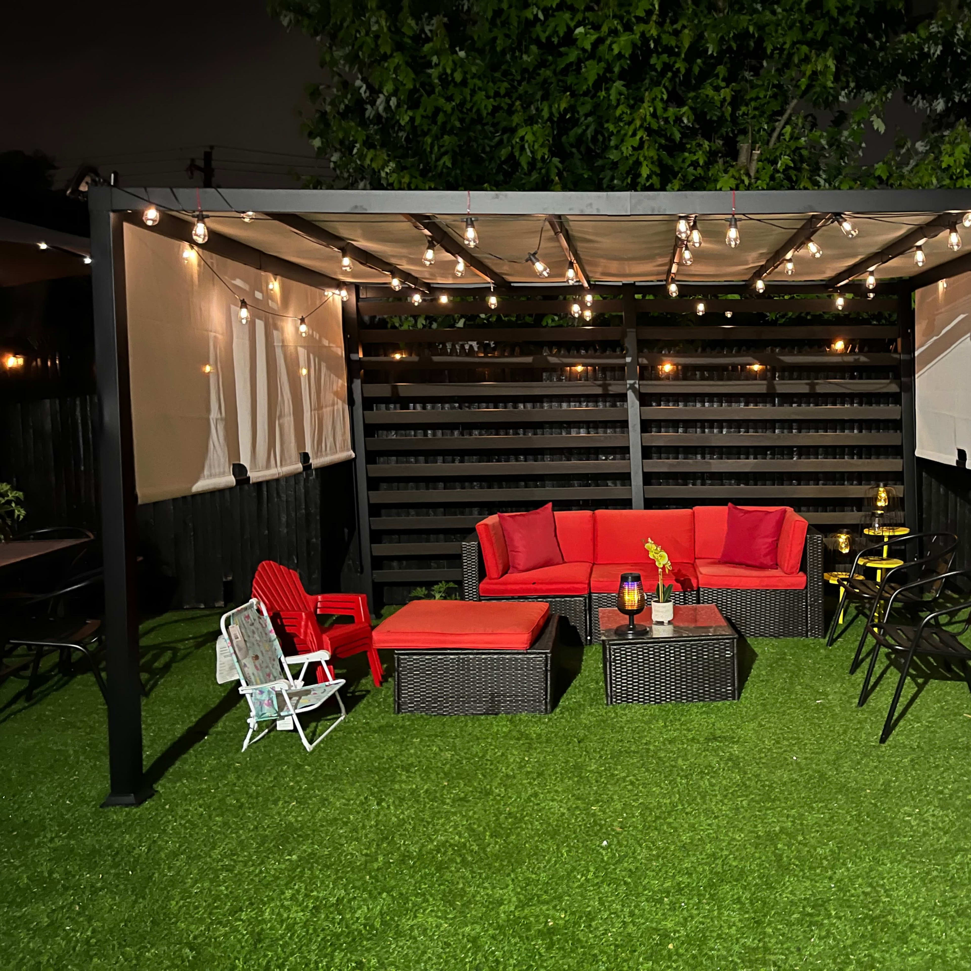 A covered outdoor seating area features red furniture, string lights, and a green artificial lawn.