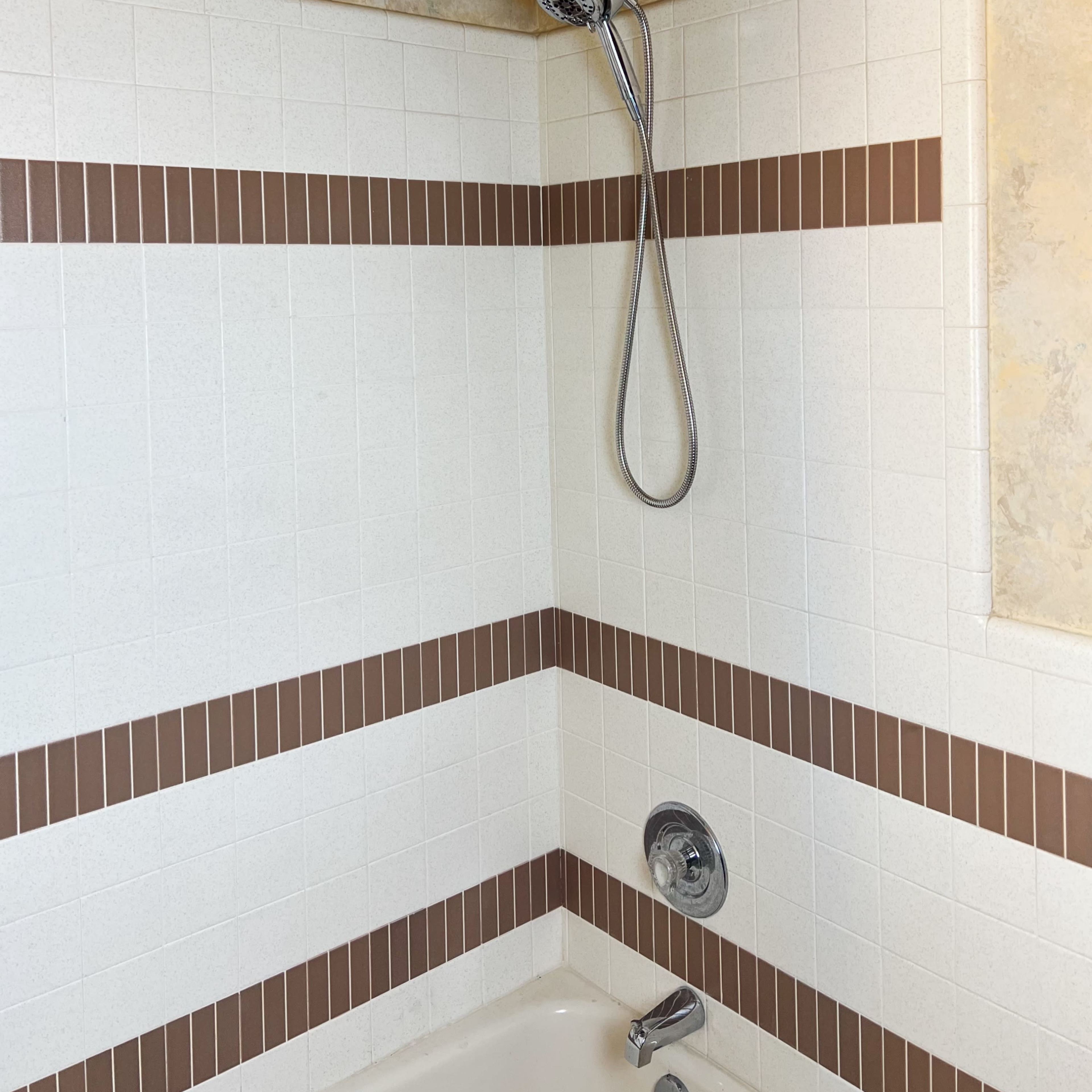 A showerhead mounted on a wall with tiled accents in a bathroom setting.