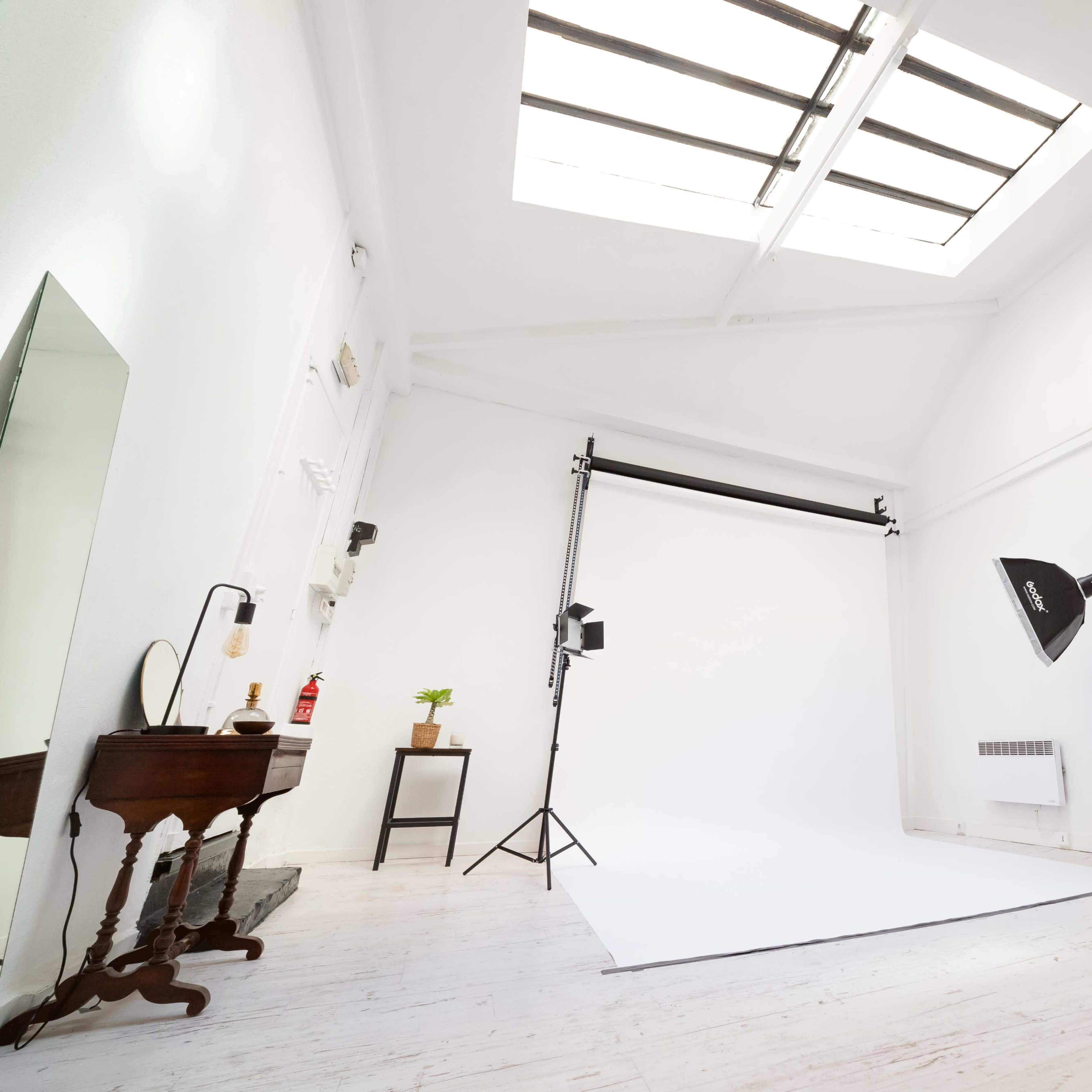 A bright photography studio features a white backdrop, lighting equipment, and minimal furnishings.