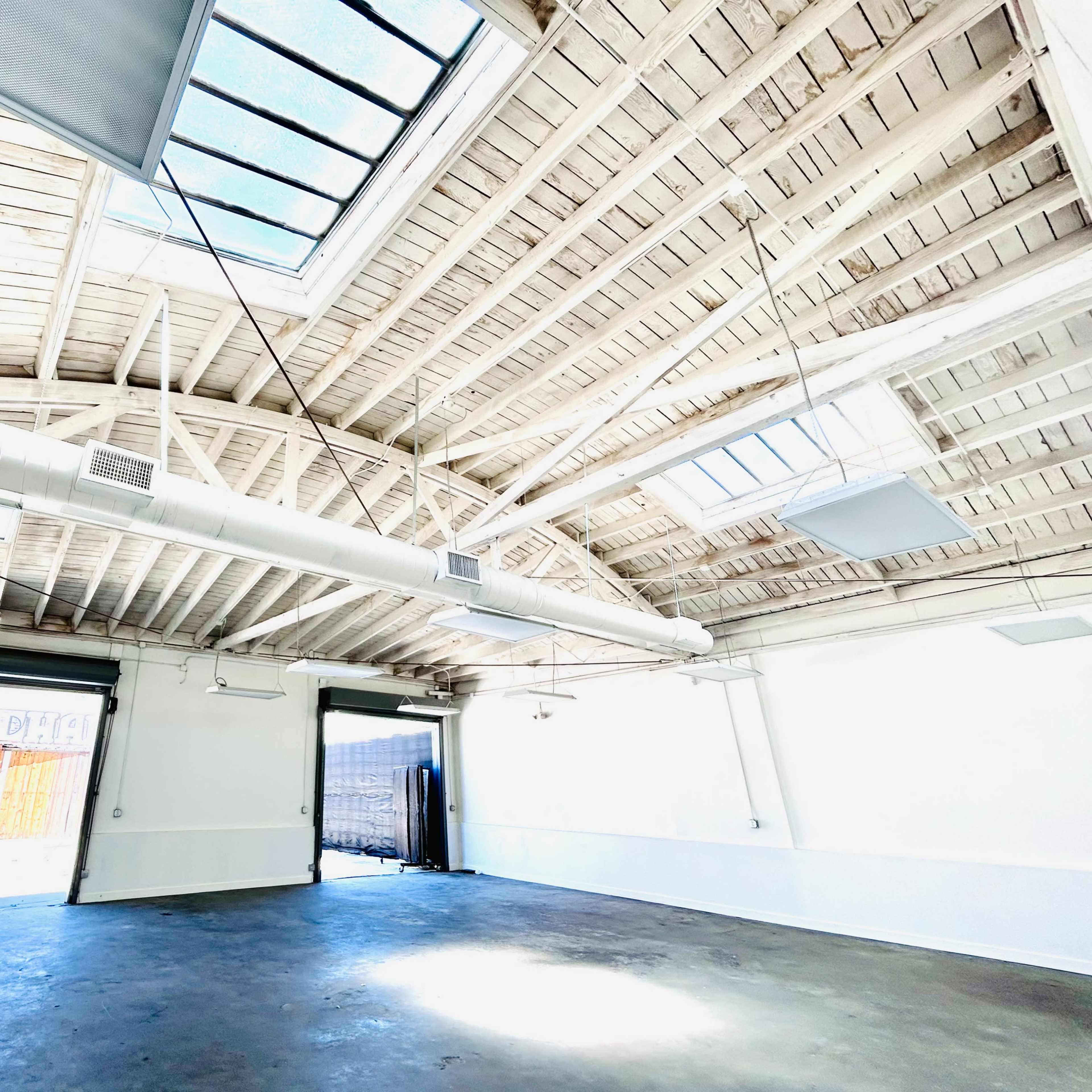 A spacious, well-lit interior of a building with wooden beams and large skylights.
