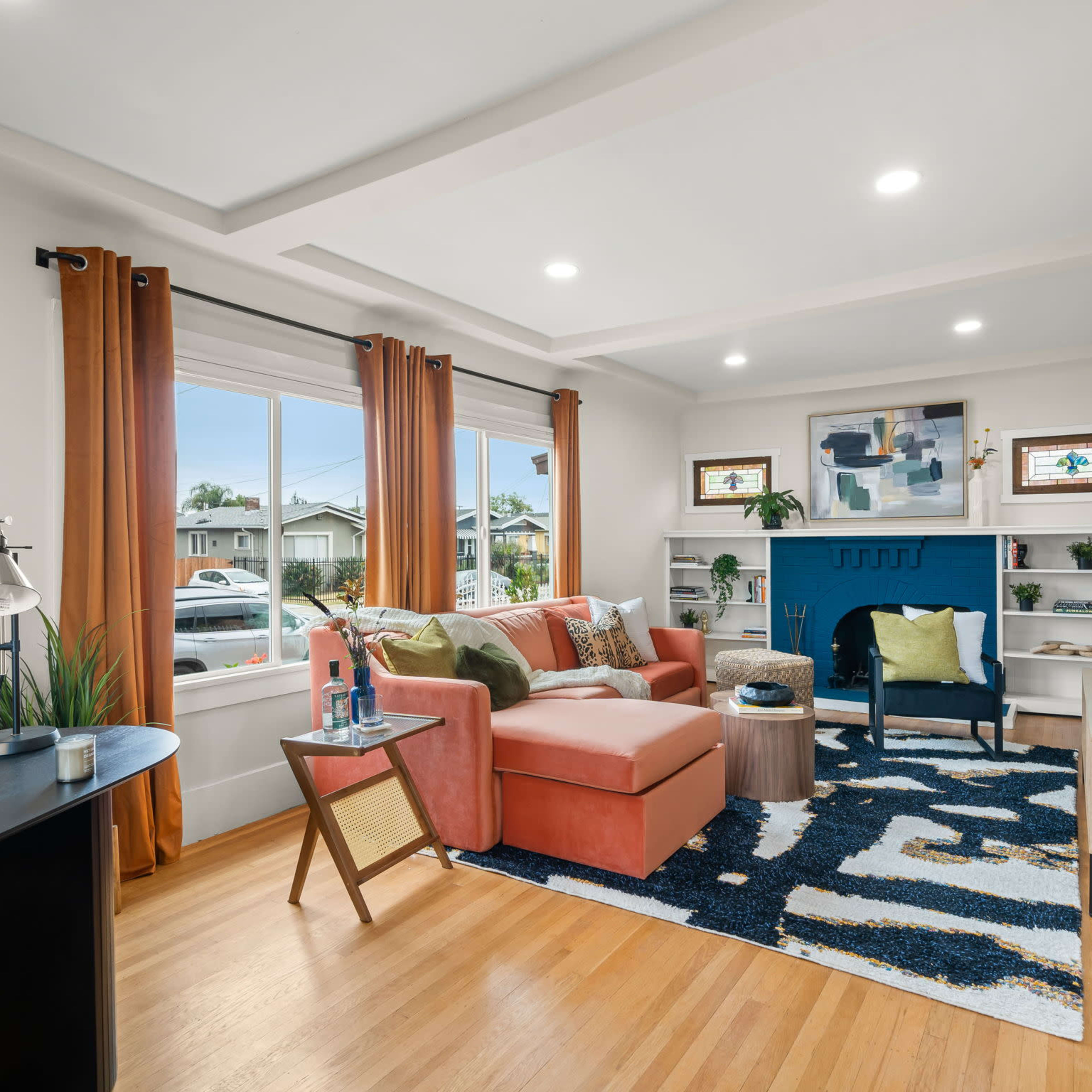 The living room features a coral sofa, blue accent wall, and large windows with orange curtains, along with a wooden coffee table and patterned rug.