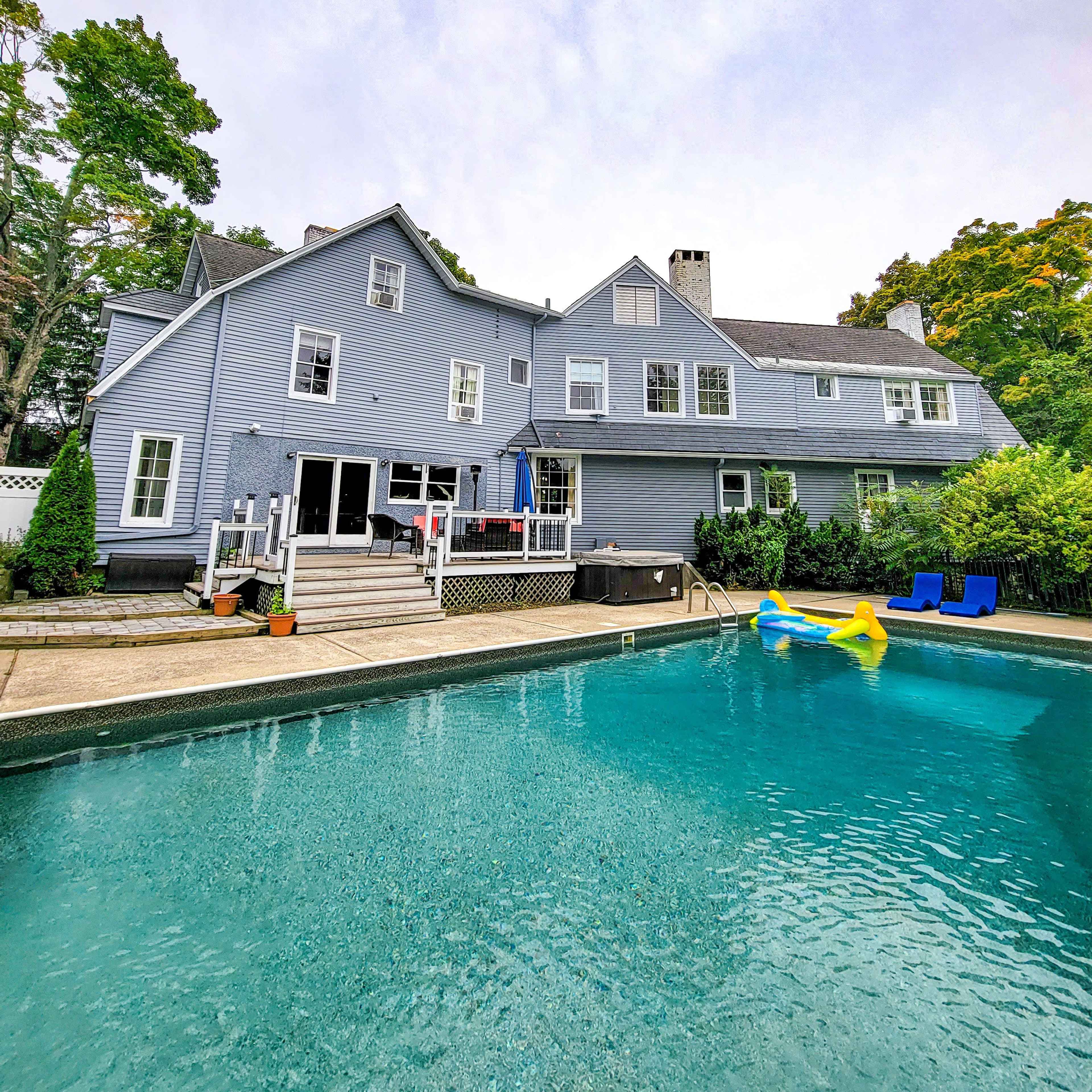 A light blue house with multiple stories and a backyard pool is visible, featuring lounge chairs and a pathway leading to the pool.
