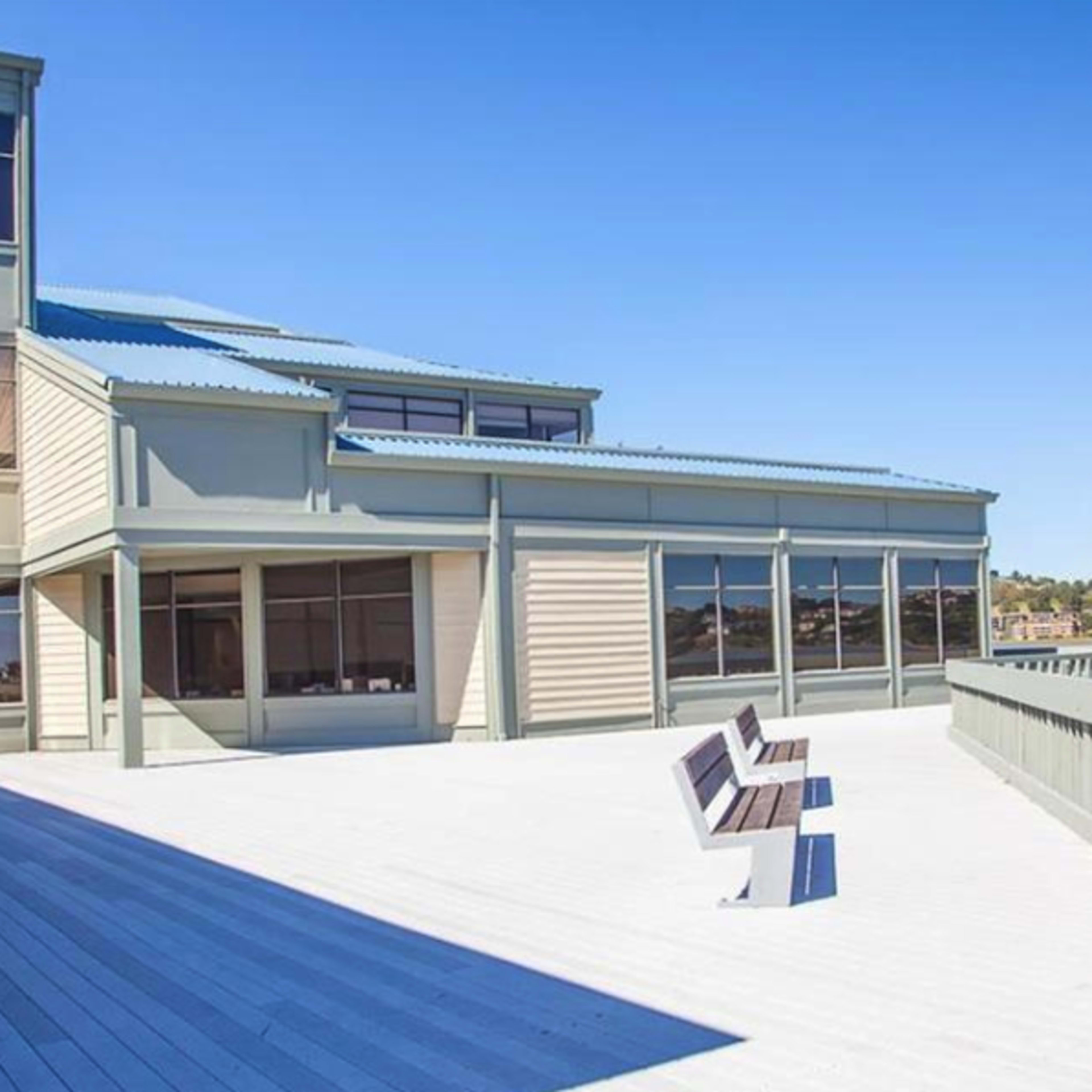 A deck with two benches overlooks a body of water, adjacent to a multi-story building with large windows.