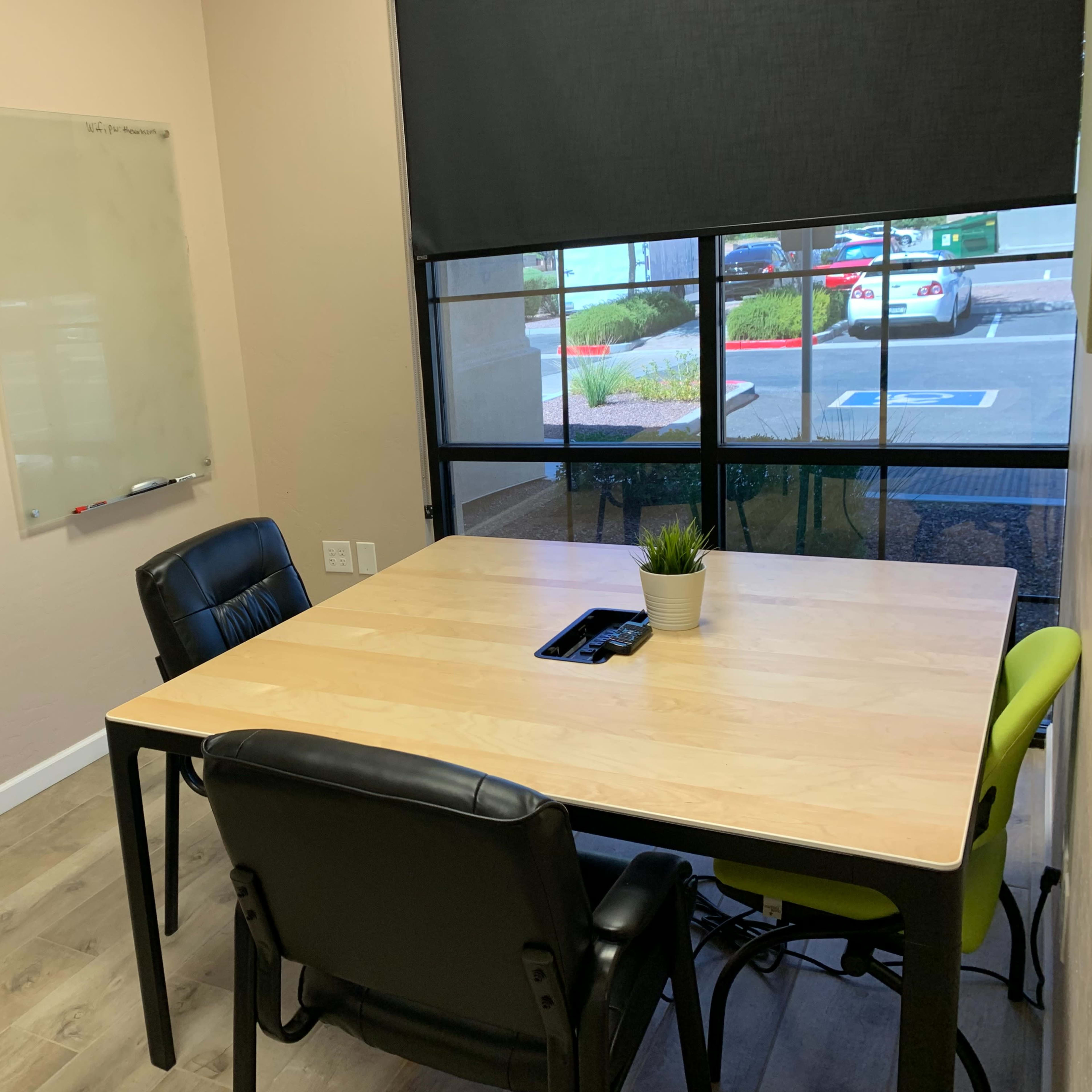 A meeting room features a wooden table with four chairs, a wall-mounted television, and a whiteboard.
