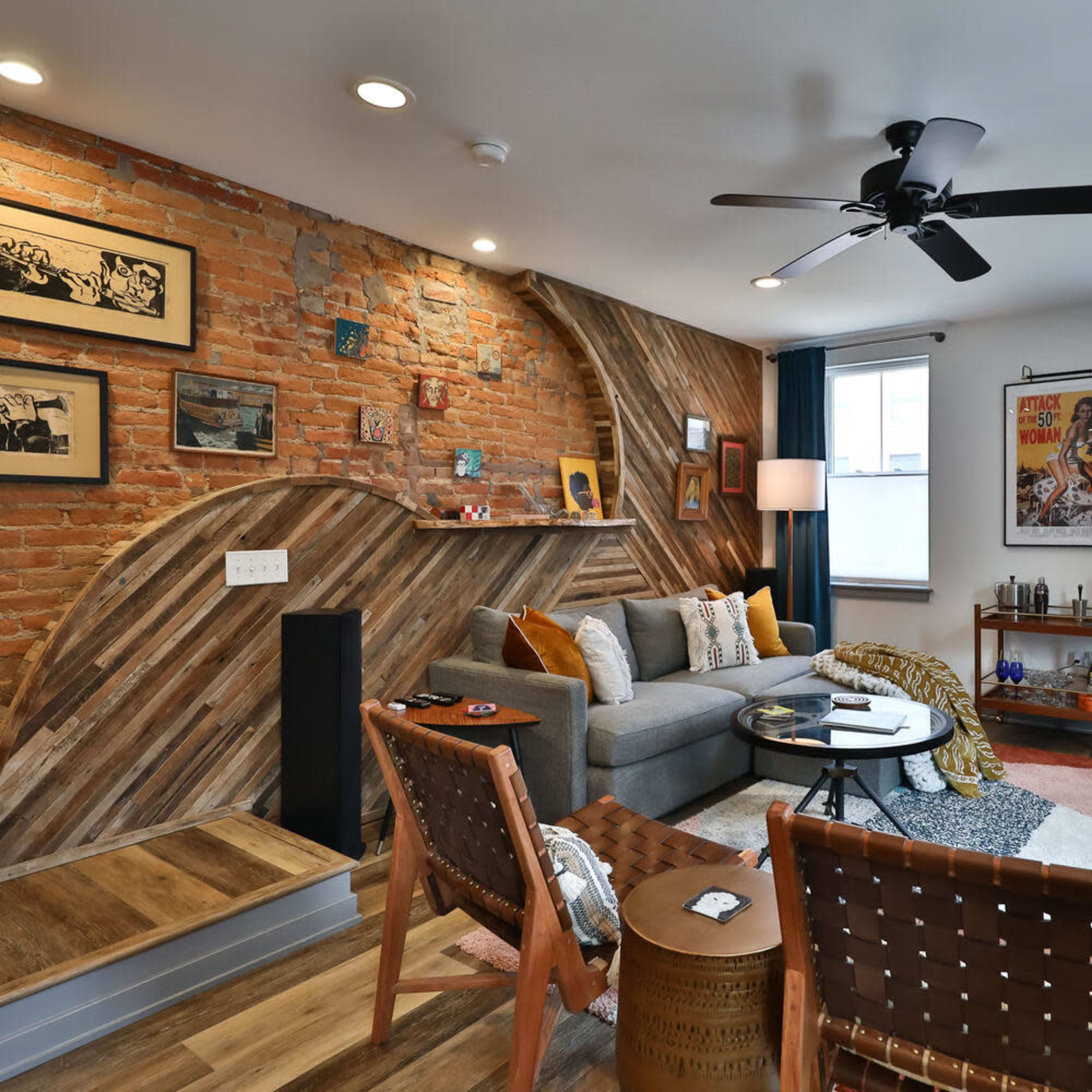 The living room features a brick wall, a grey sofa, and a mix of decorative furniture arranged around a geometric area rug.