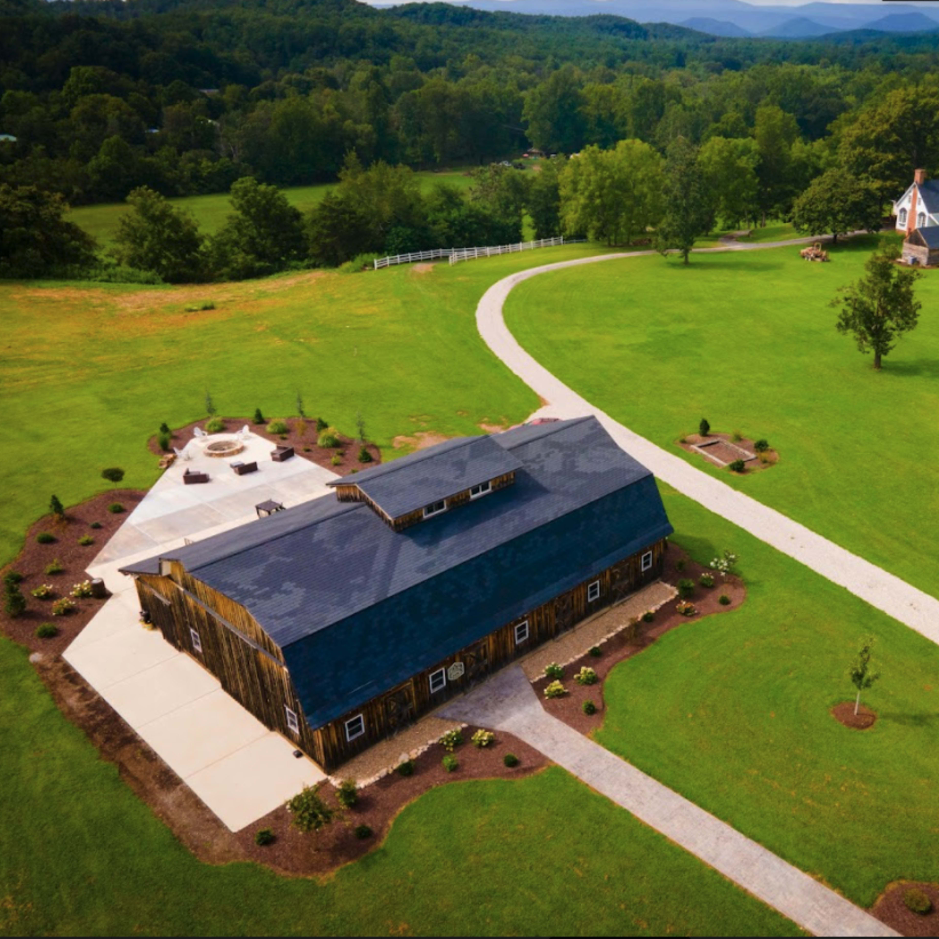 An expansive green landscape featuring a large barn-like structure, a winding pathway, and a house with a white exterior in the background.