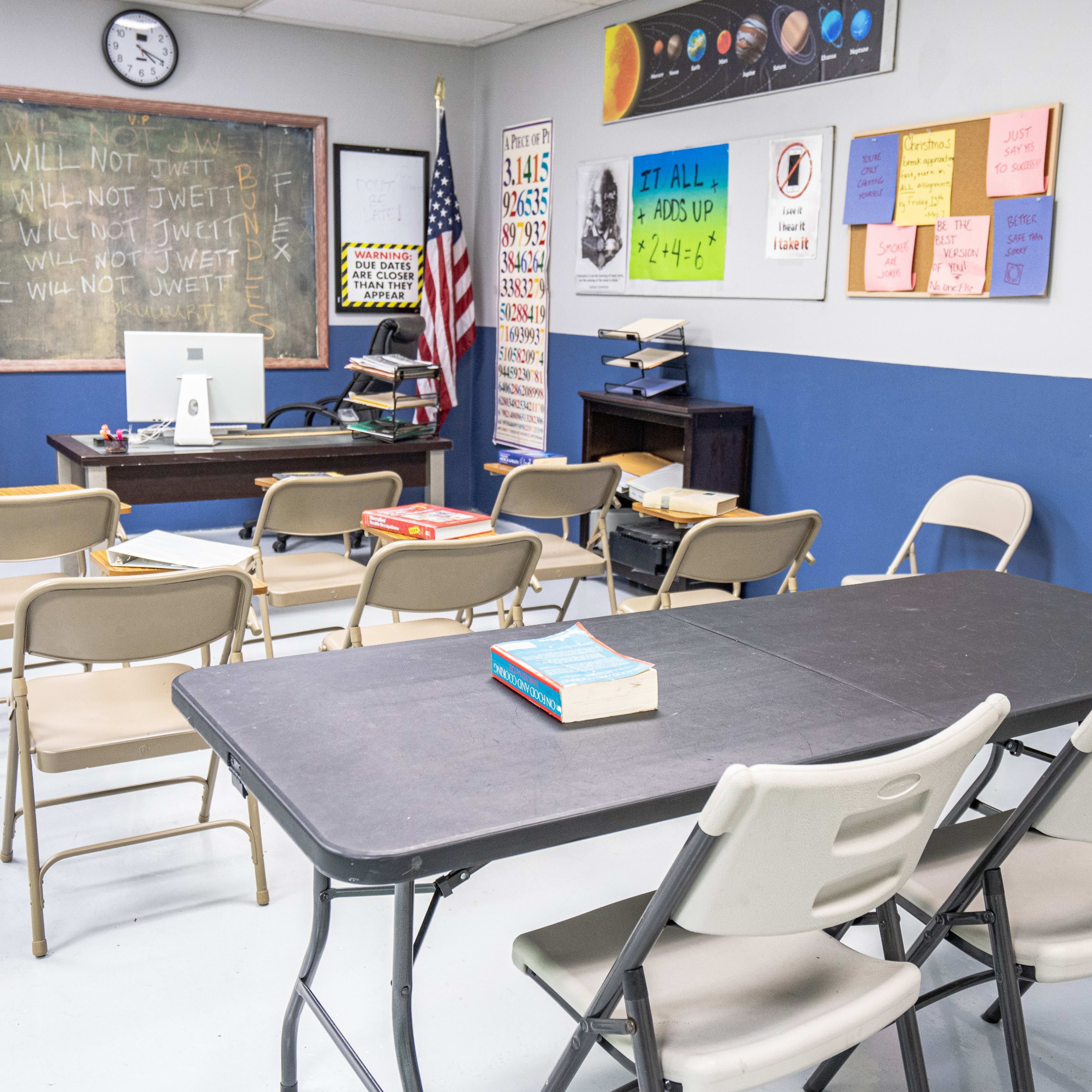A classroom with a blackboard, desks arranged in rows, a computer, and educational posters on the walls.