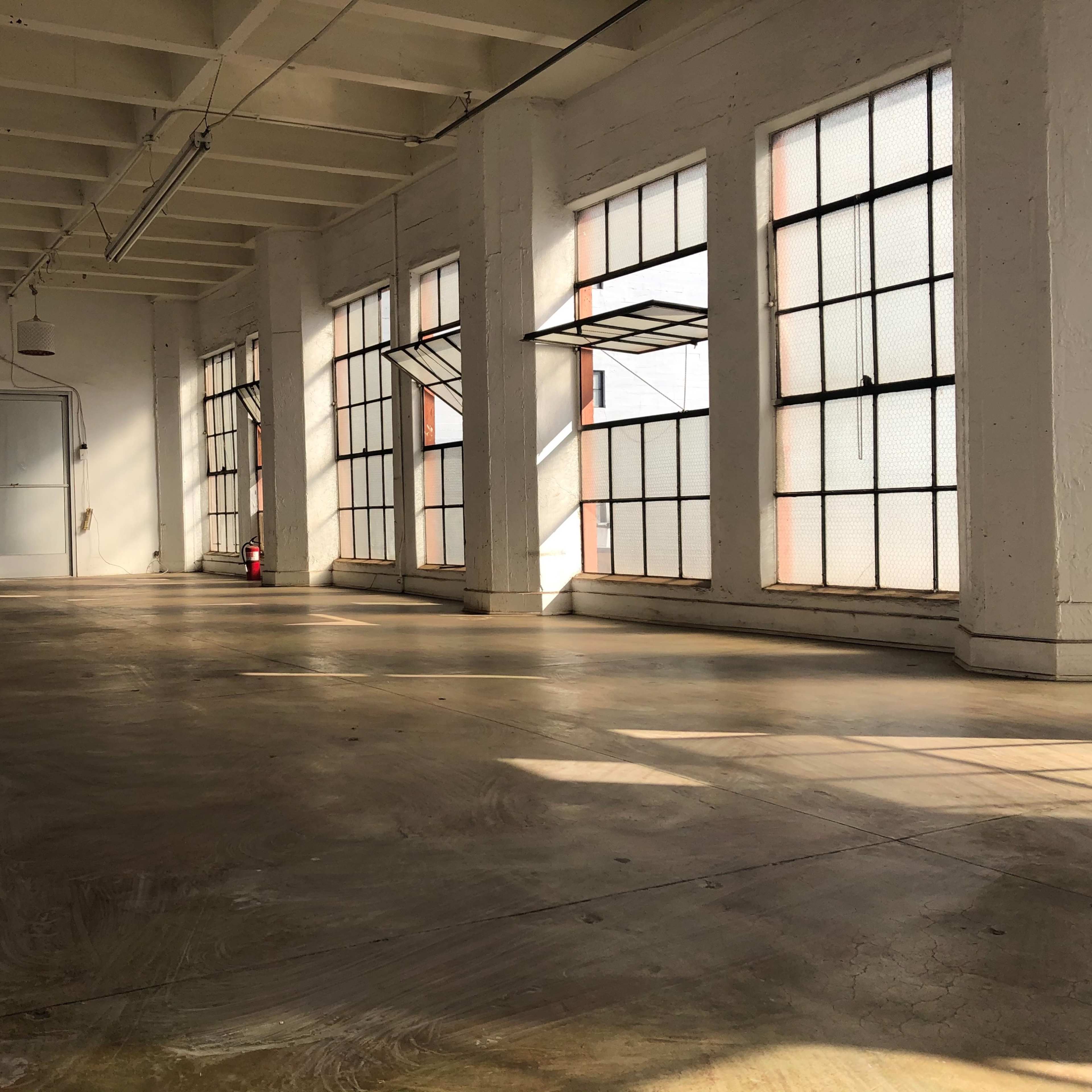 A spacious, empty room with large windows and concrete flooring.