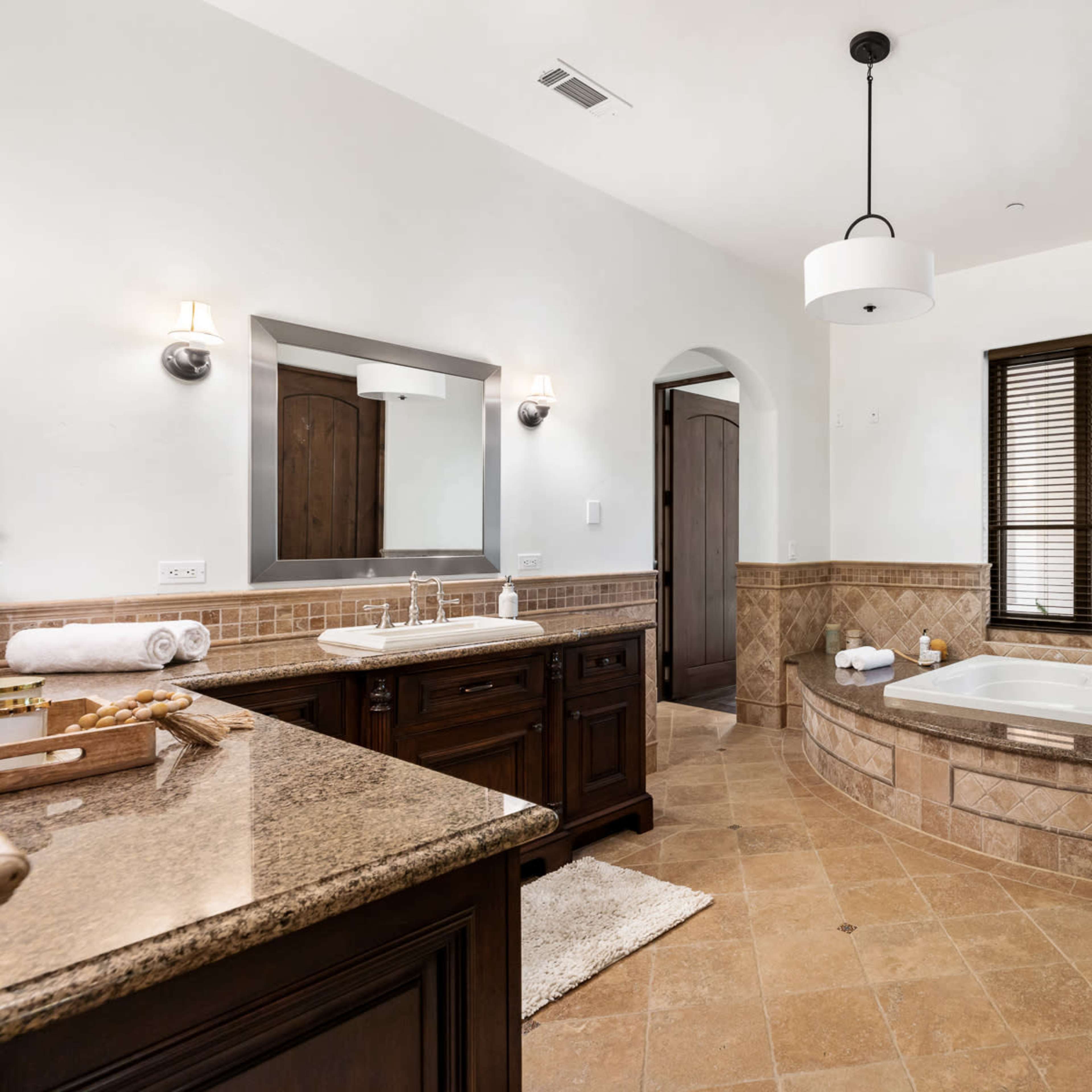 A spacious bathroom features a large soaking tub, a double vanity with a mirror, and a window with wooden blinds.
