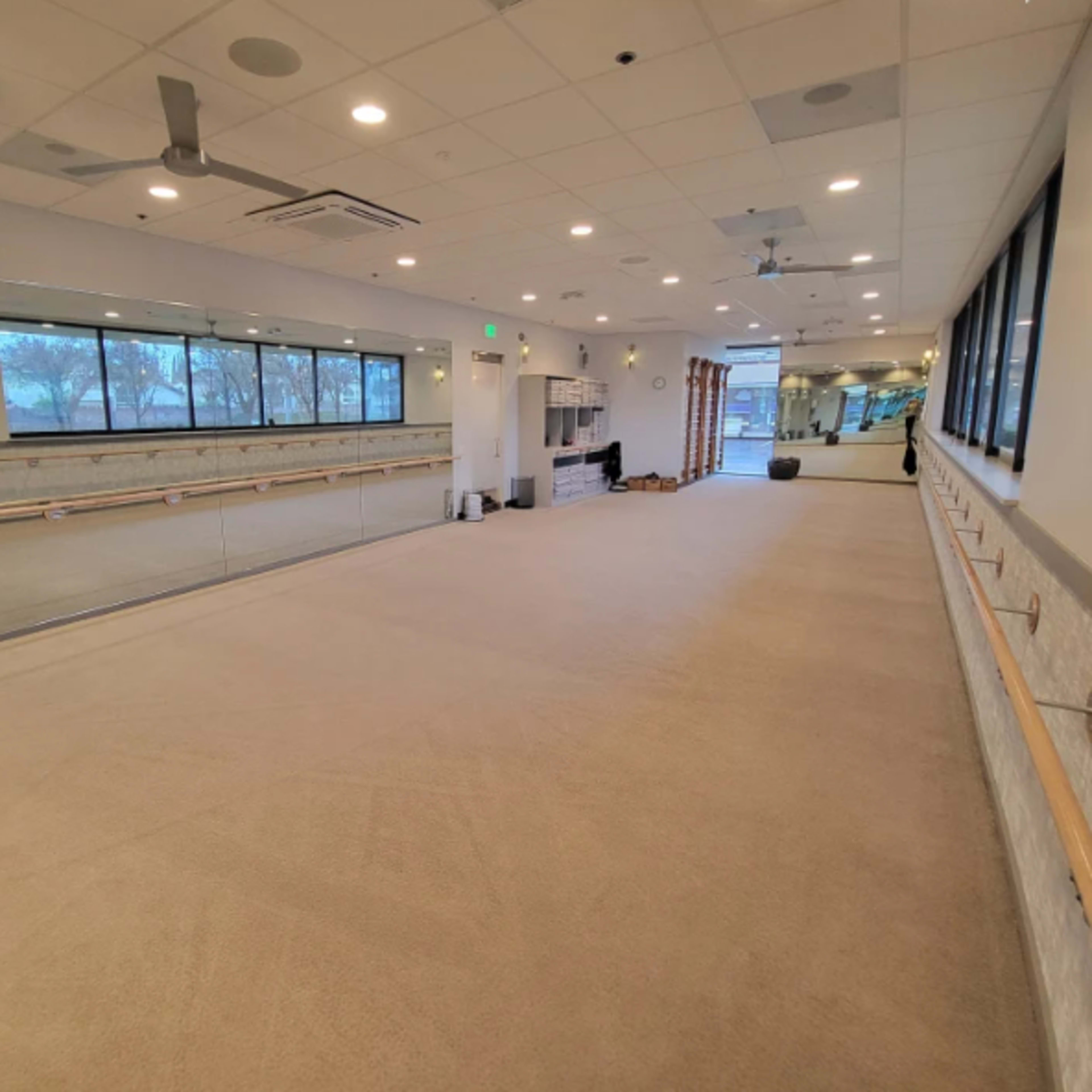 An empty fitness studio with mirrors along one wall and a barre installed across the room.
