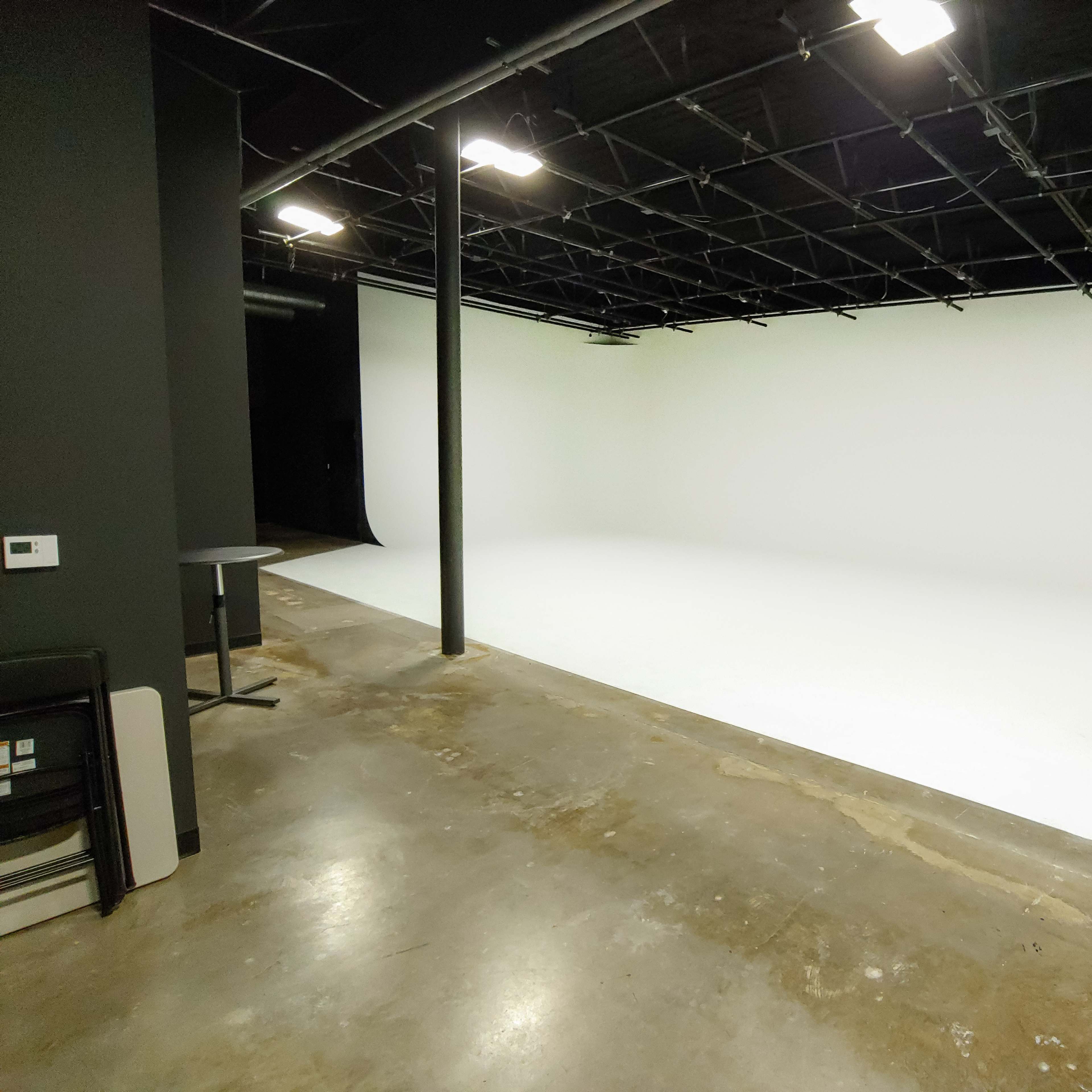 A spacious photography studio with a seamless white backdrop and exposed lighting infrastructure.