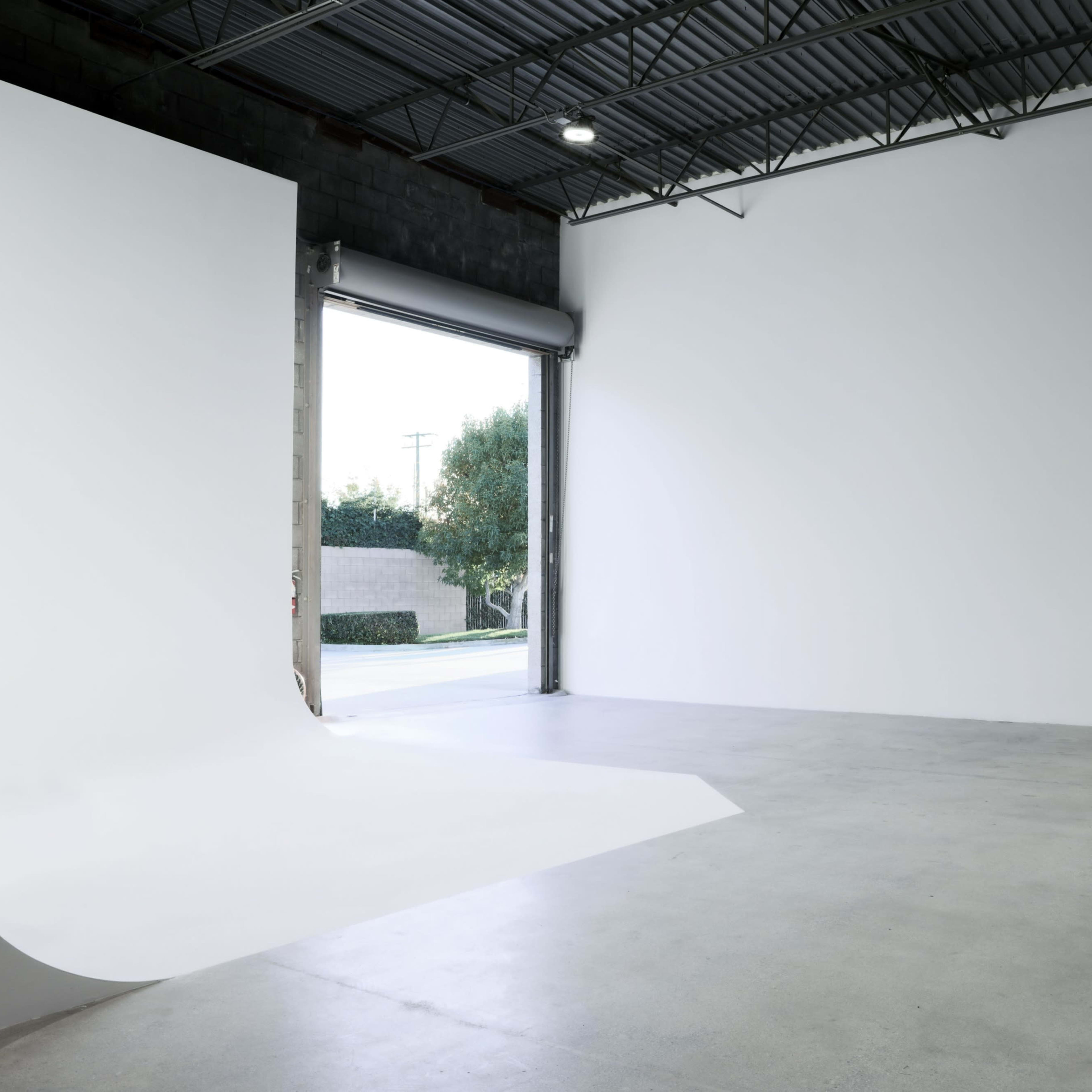 A spacious, empty room with a smooth white backdrop and an open door leading to a view of the outdoors.